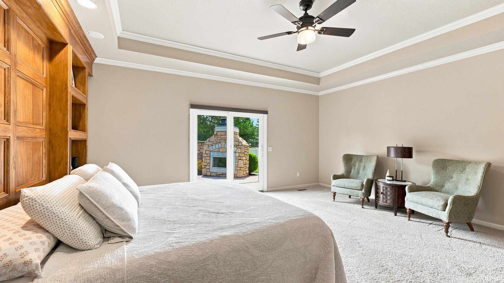 Spacious room featuring a tray ceiling with crown molding, ceiling fan, built-in wood cabinetry, and glass patio doors leading to an exterior stone fireplace