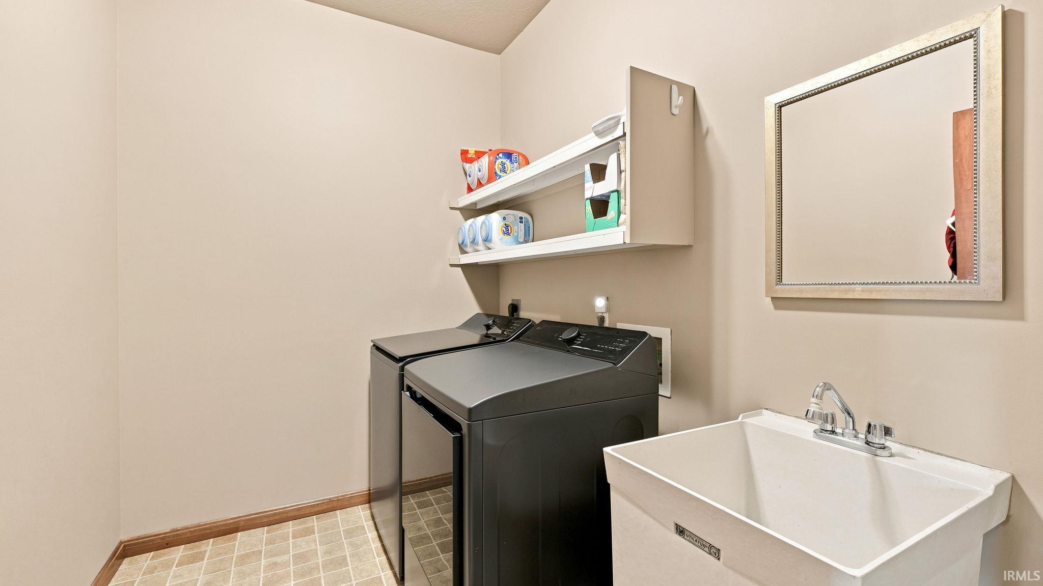 Dedicated laundry area featuring modern appliances, wall-mounted shelving, a utility sink with chrome faucet, a framed mirror, and diamond-patterned flooring
