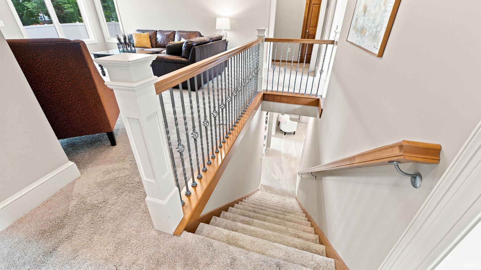 Carpeted staircase with light wood handrails and decorative wrought iron balusters