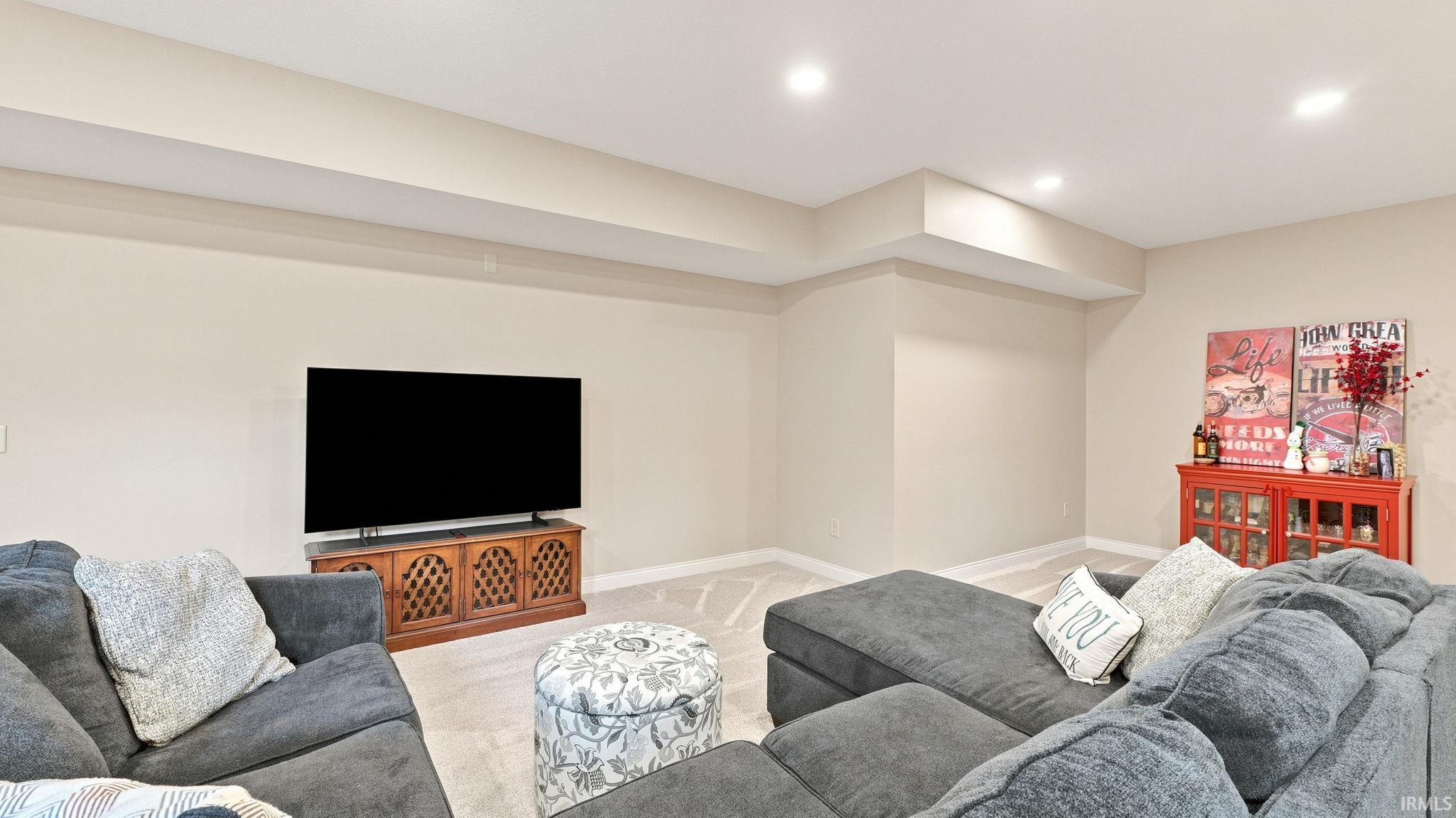 Spacious recreation room featuring neutral wall paint, recessed lighting, and carpet flooring with a geometric pattern