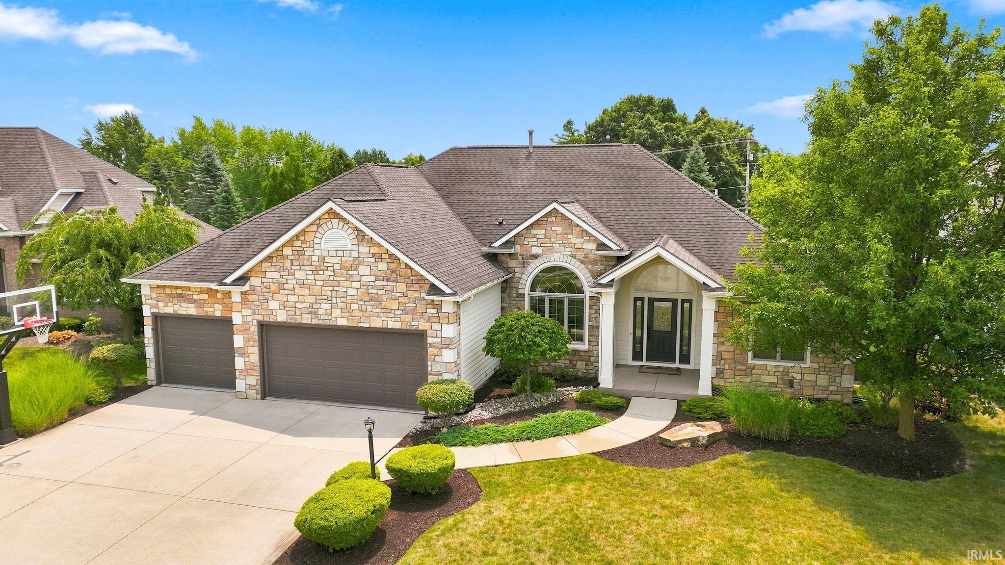 Stone and siding exterior featuring a three-car garage, concrete driveway, and a curved walkway to the entry