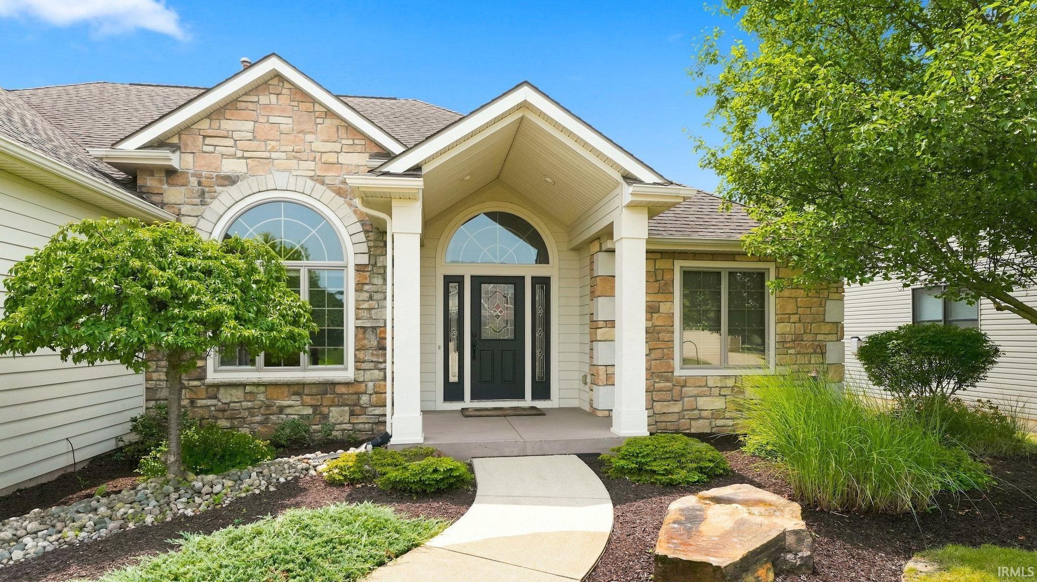 Stone and siding exterior with a prominent arched entry window and a covered front porch featuring square columns