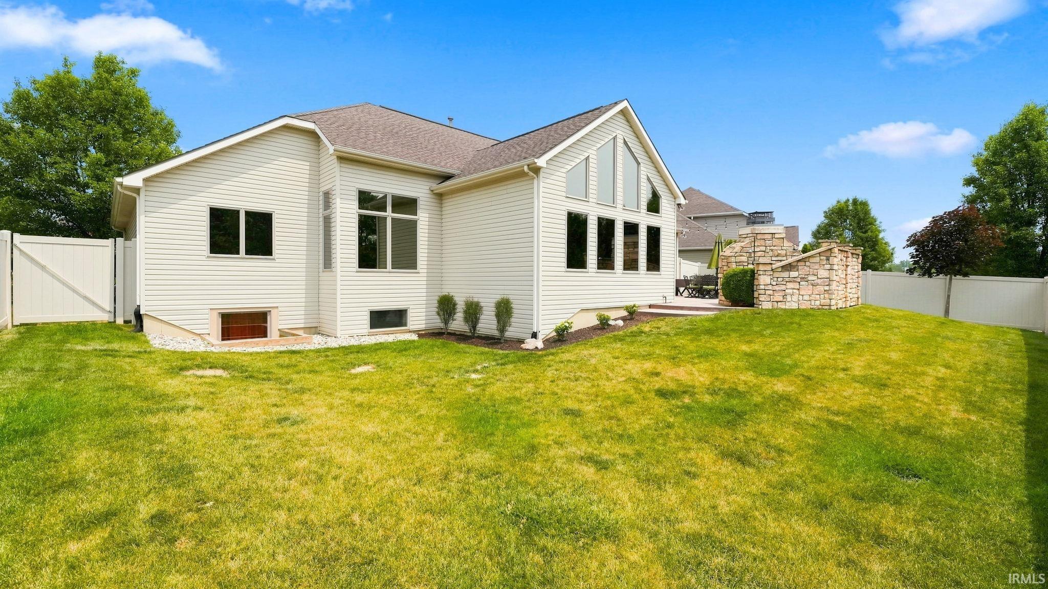 Expansive lawn area featuring a privacy fence, a stone-clad outdoor fireplace, and a patio space
