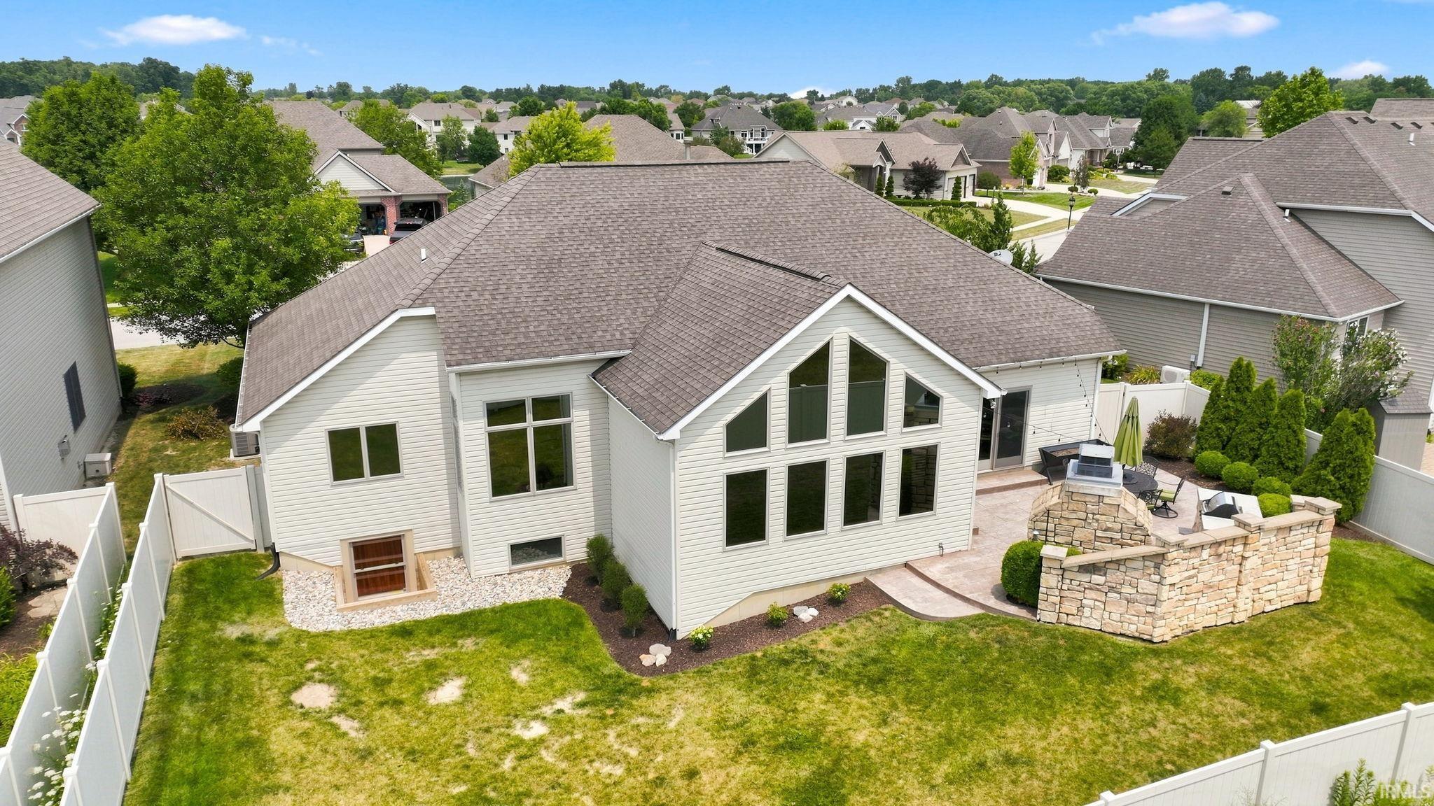Rear exterior featuring an expansive paver patio with a stone privacy wall, a fenced yard, and large-pane windows with architectural details