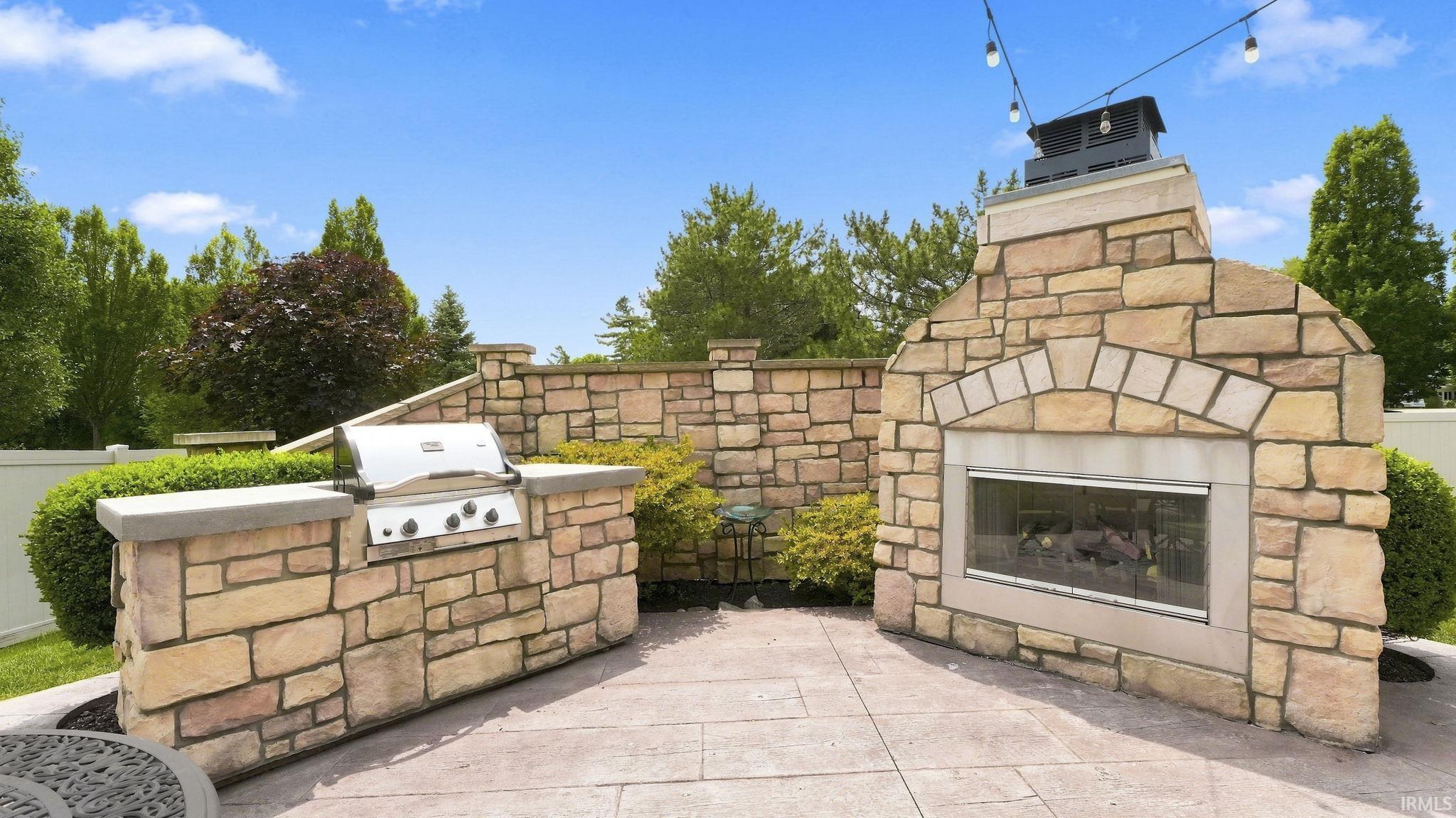 Expansive outdoor living area featuring a stone fireplace, built-in BBQ, stone privacy wall, and string lighting