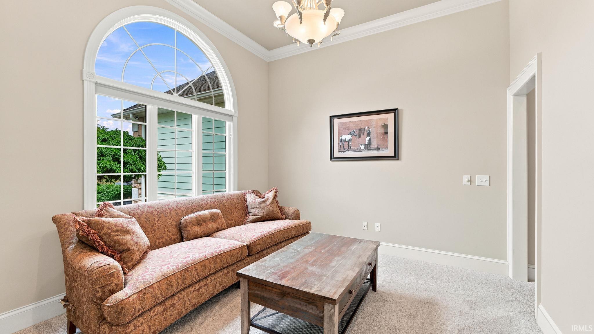 Arched window with gridded panes, high ceilings, crown molding, and carpeted flooring