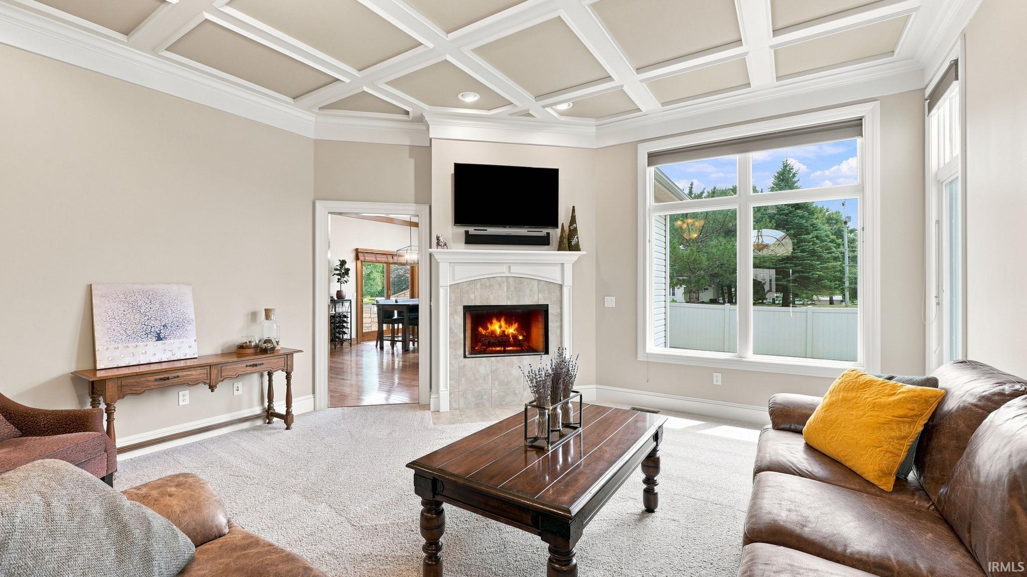 Living space featuring a coffered ceiling, gas fireplace with tile surround, large picture windows, and light-toned carpet flooring