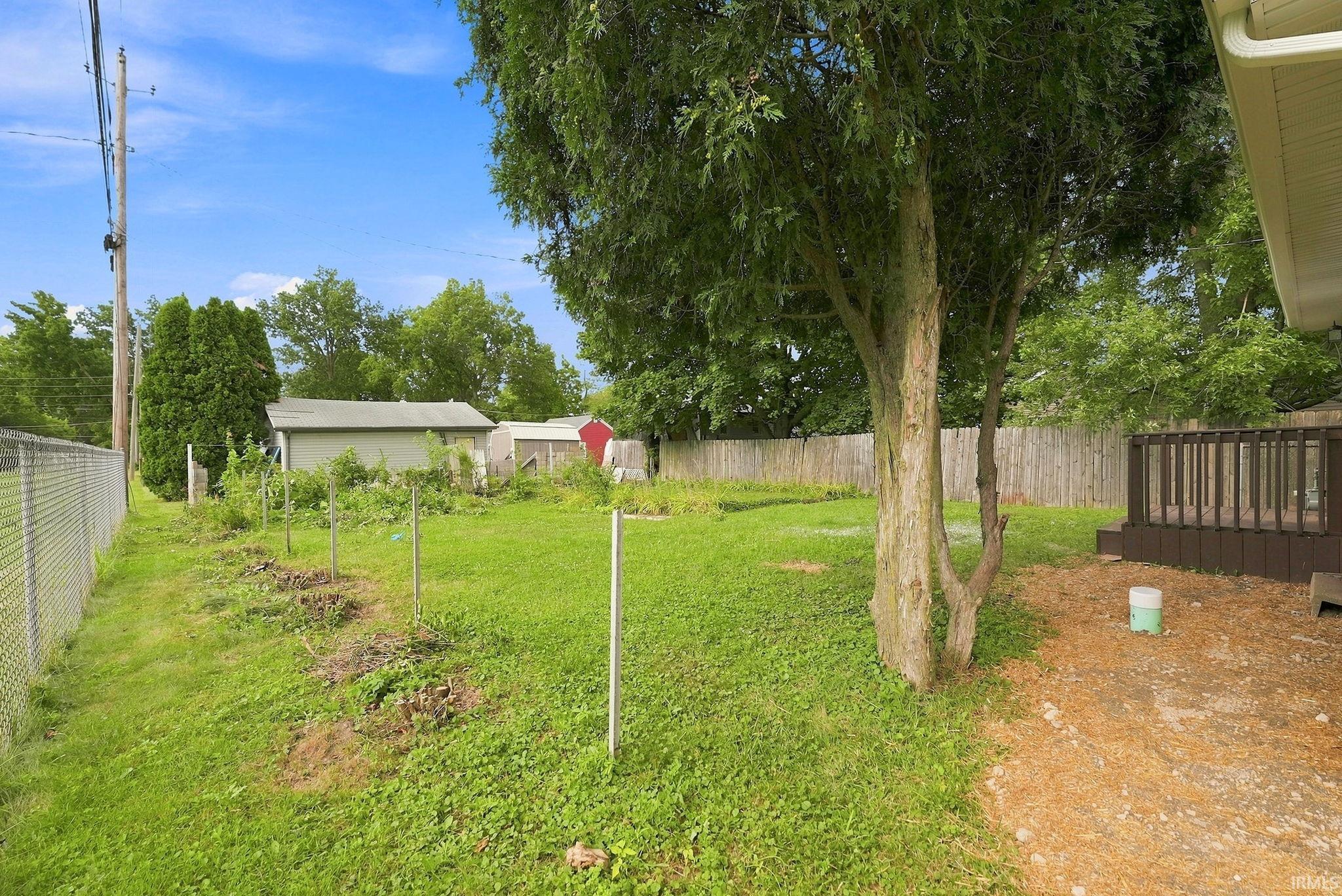Spacious backyard with a chain-link fence, mature trees, and a raised wood-finish deck