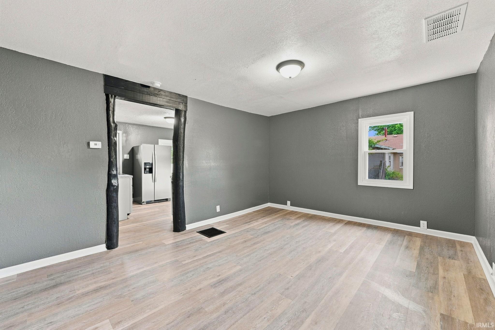 Spacious room featuring light wood-finish flooring, neutral gray walls, a white trim baseboard, and a contrasting dark wood-framed doorway