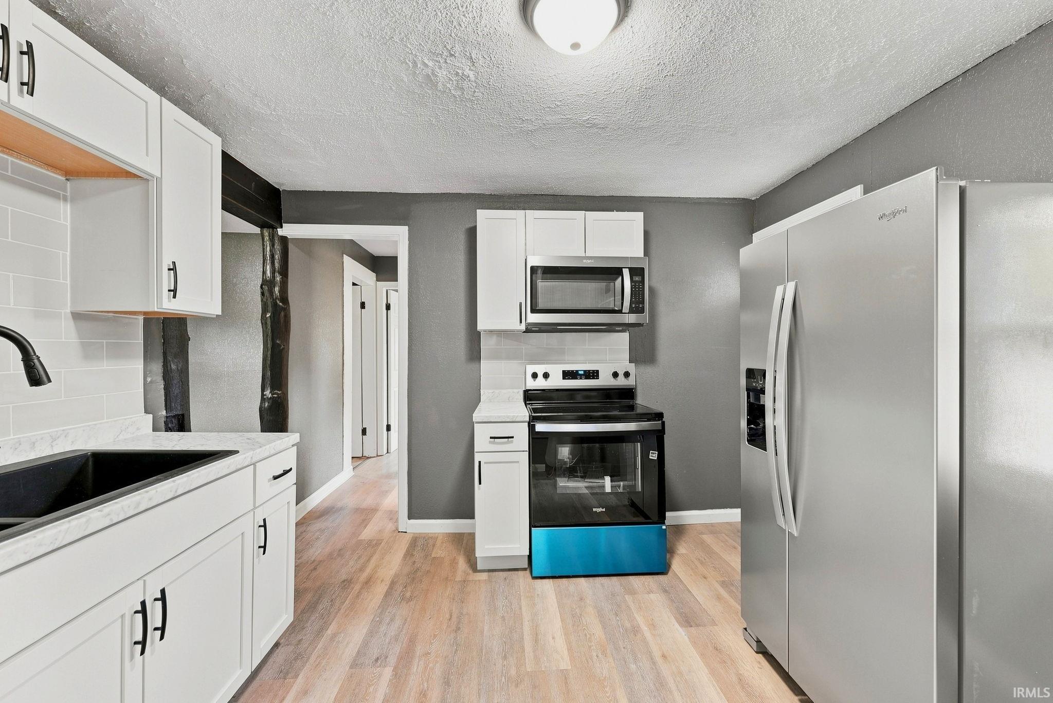 Contemporary kitchen featuring white cabinetry, light countertops, and wood-finish flooring