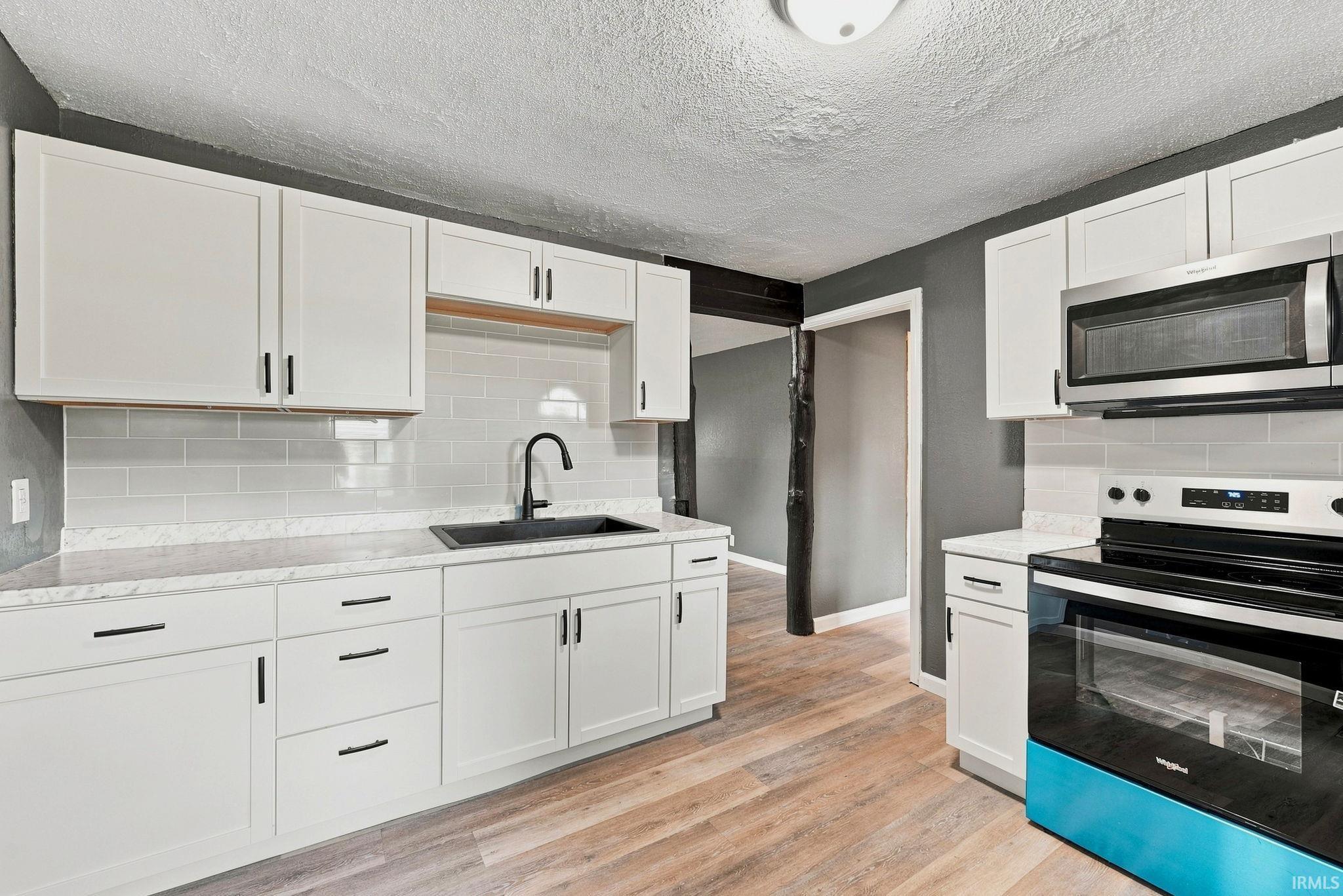 Contemporary kitchen featuring white cabinetry, light countertops, a subway tile backsplash, stainless steel appliances, and wood-finish flooring