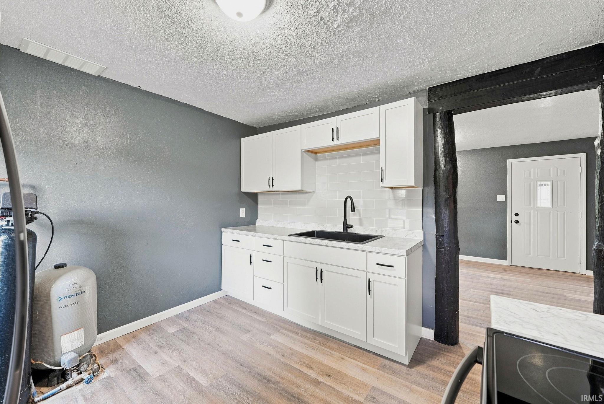 Kitchenette featuring white shaker-style cabinetry, a matte black faucet, a dark basin sink, and a white subway tile backsplash