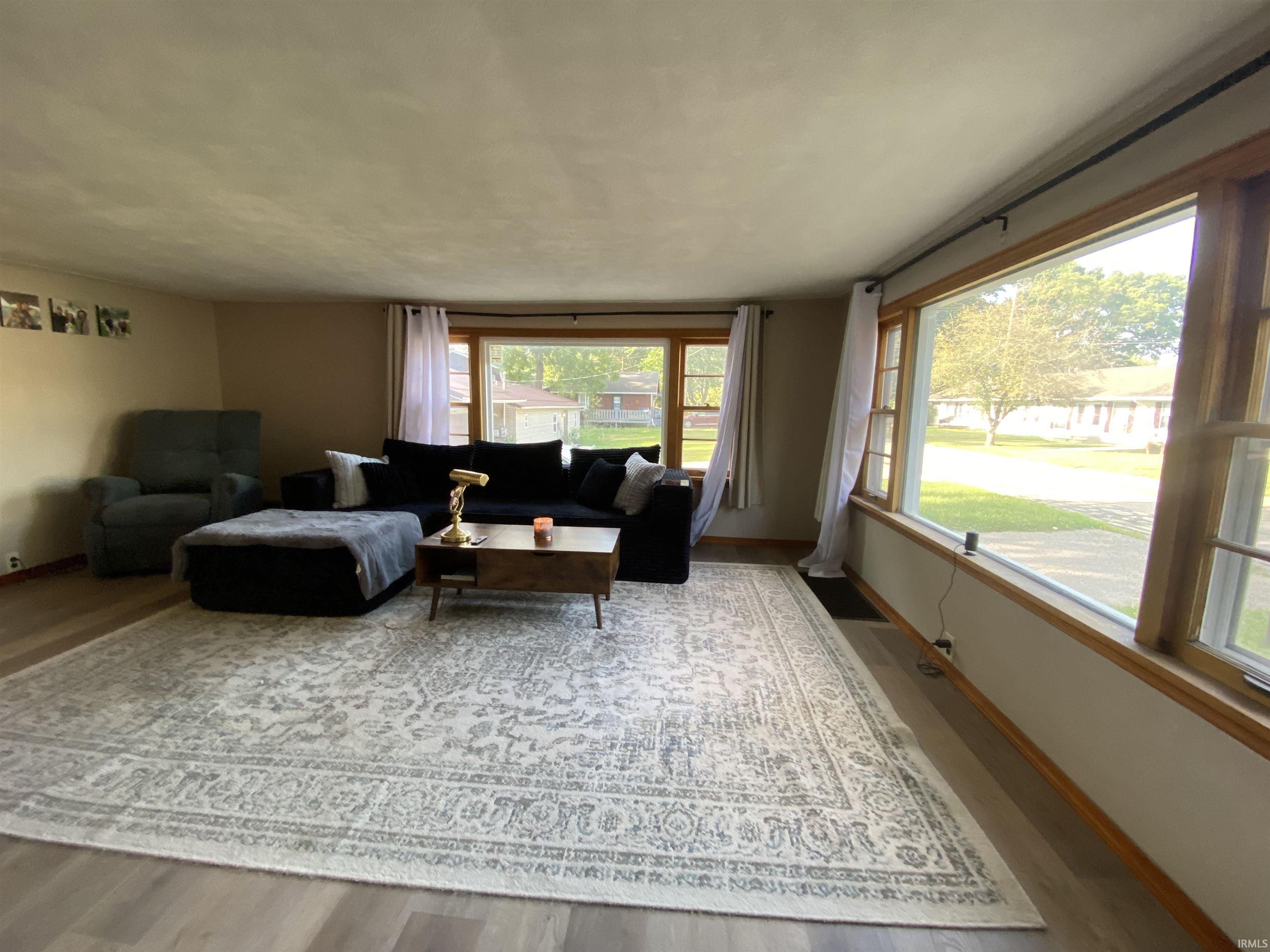 Spacious living area featuring wood-finish flooring, light-colored walls, and a large front-facing window