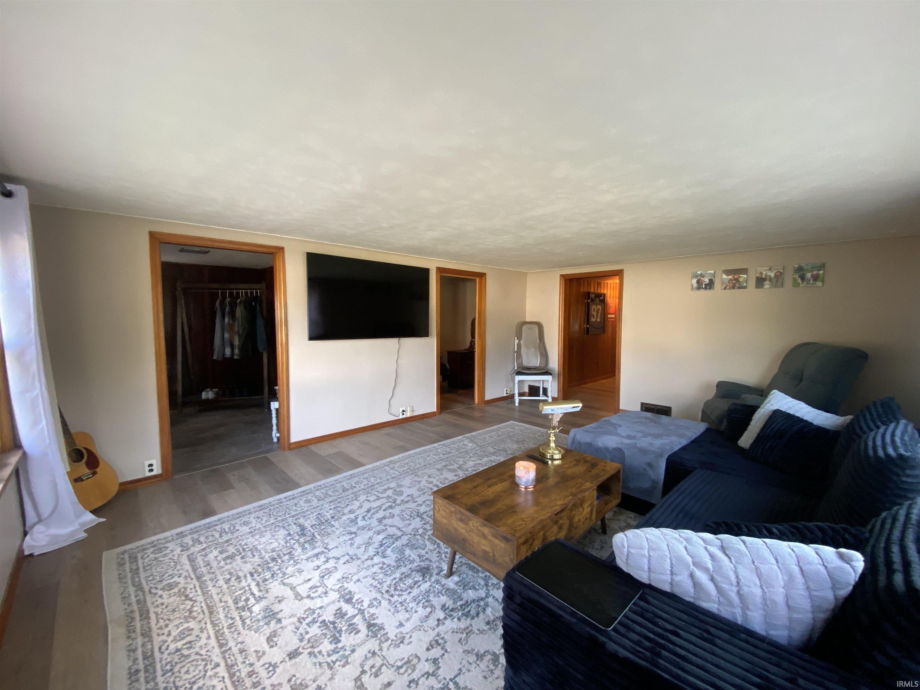 Spacious living area featuring wood-finish flooring, light-toned walls, and wood trim around doorways