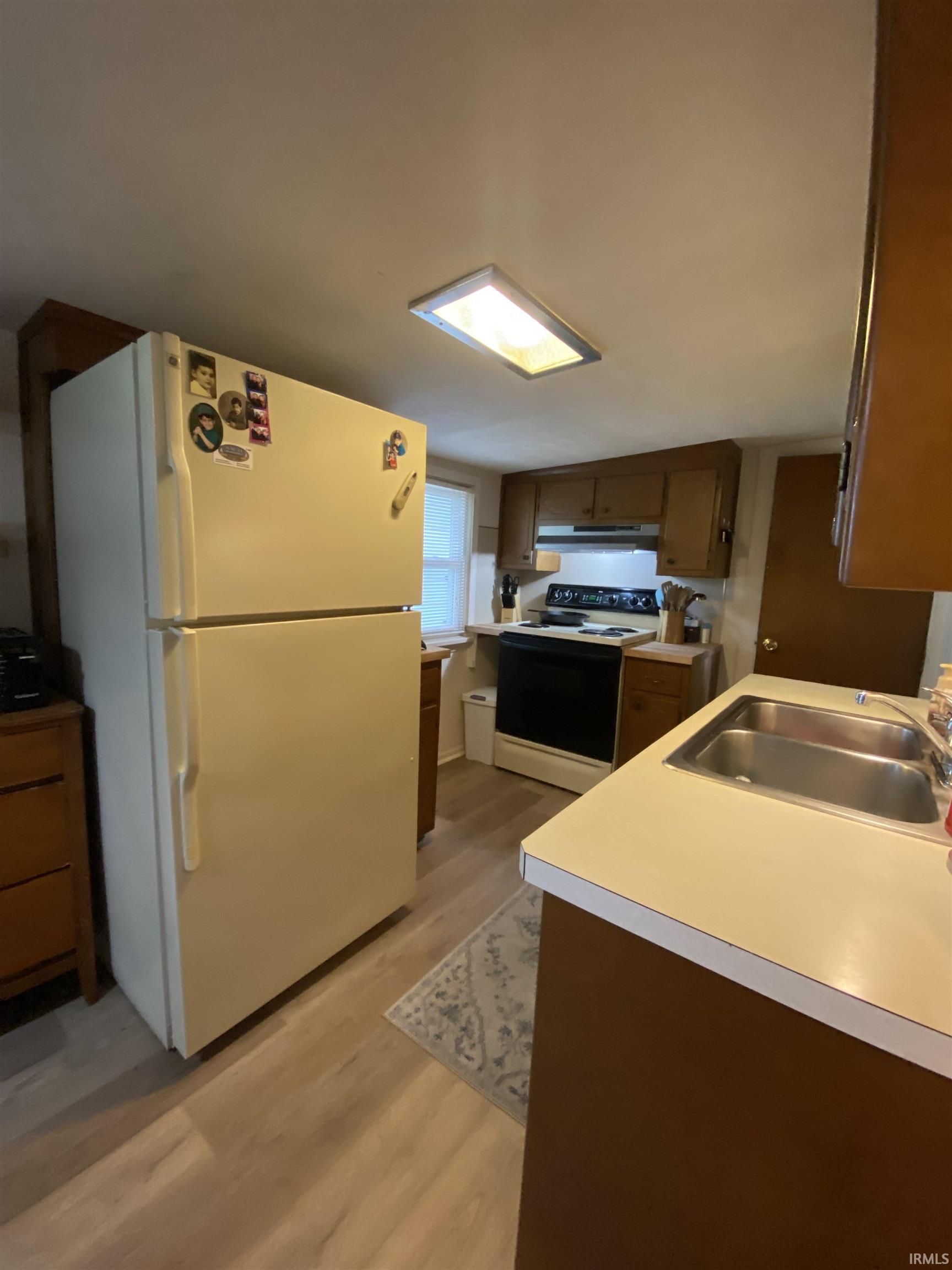 Kitchen with wood-finish flooring, built-in wooden cabinetry, double-basin stainless steel sink, and light-toned countertops
