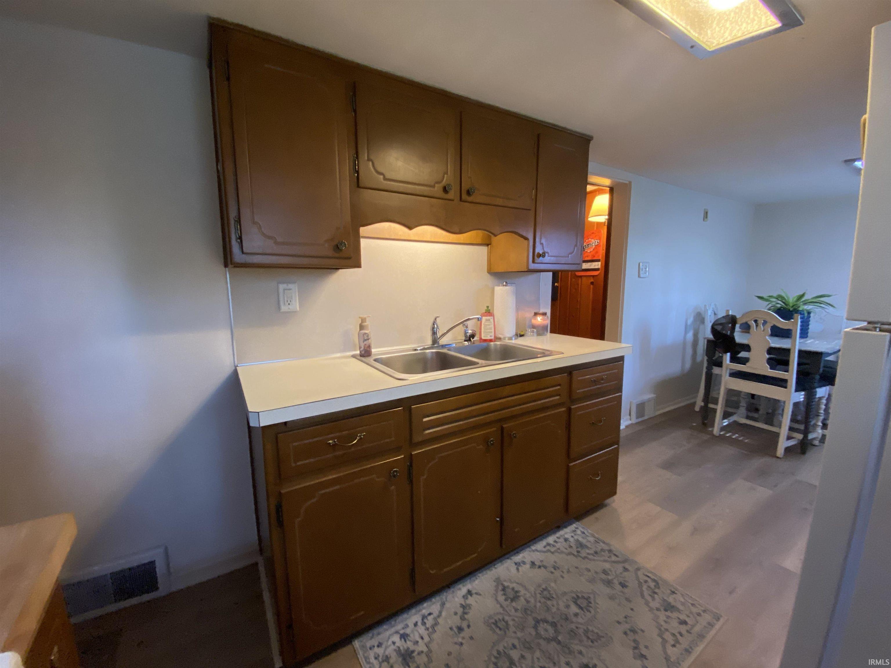 Kitchen area featuring wood-finish cabinetry, a double basin stainless steel sink, and light-toned countertops