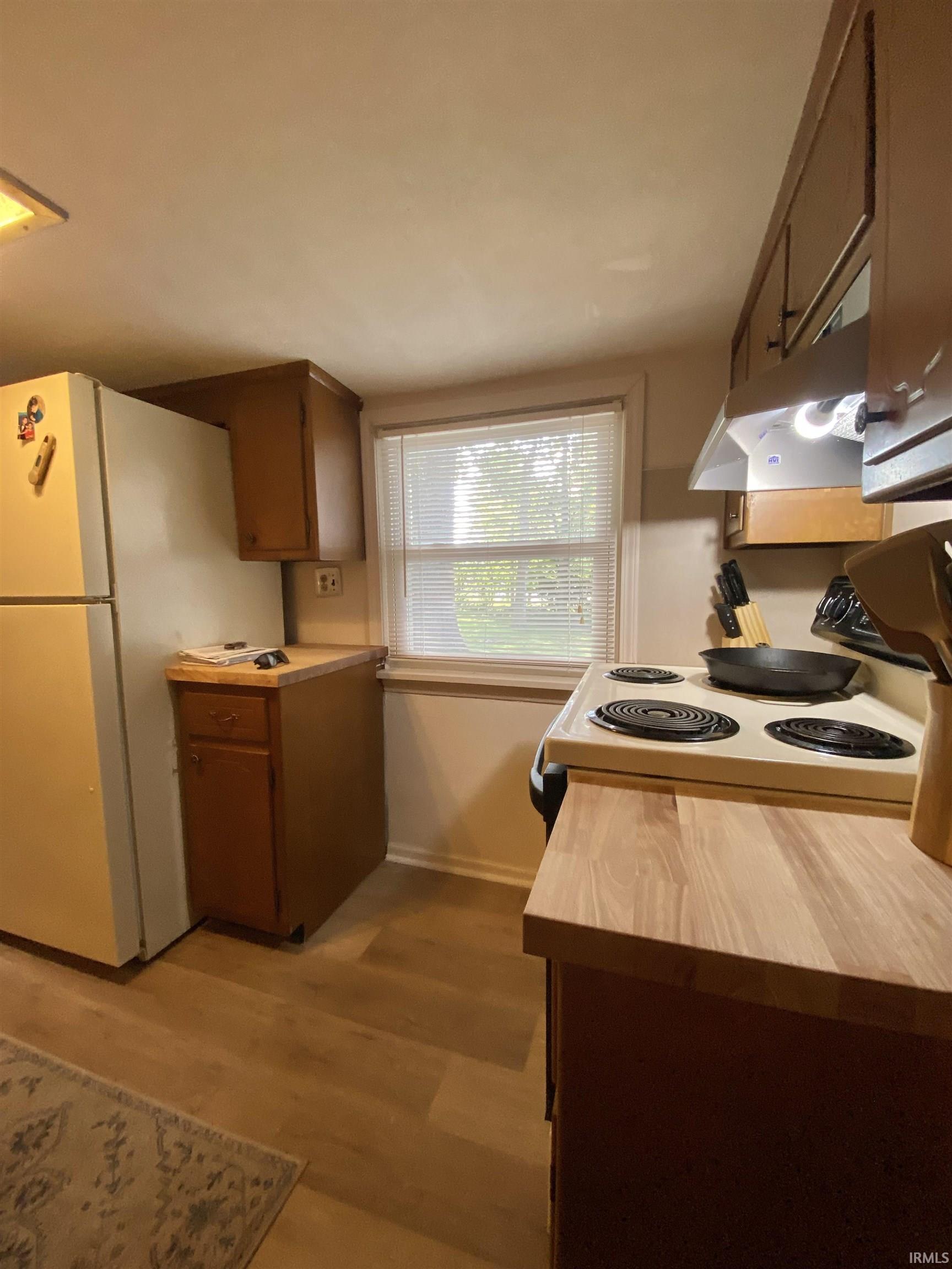 Kitchen featuring wood-finish flooring, wood cabinetry, light-toned countertops, and a window with blinds