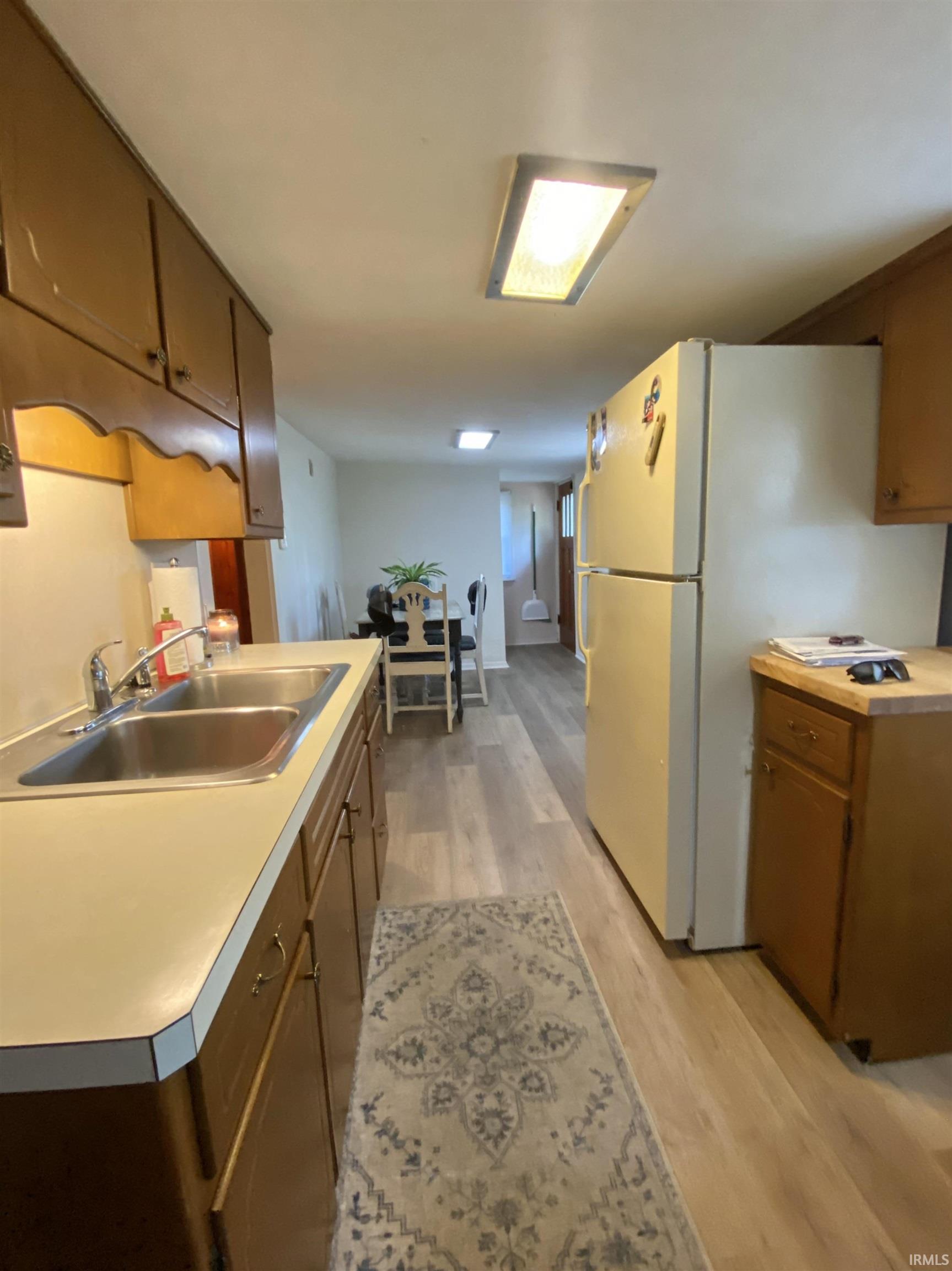 Kitchen featuring wood-finish flooring, dual basin stainless steel sink, light-colored countertops, and upper and lower cabinetry