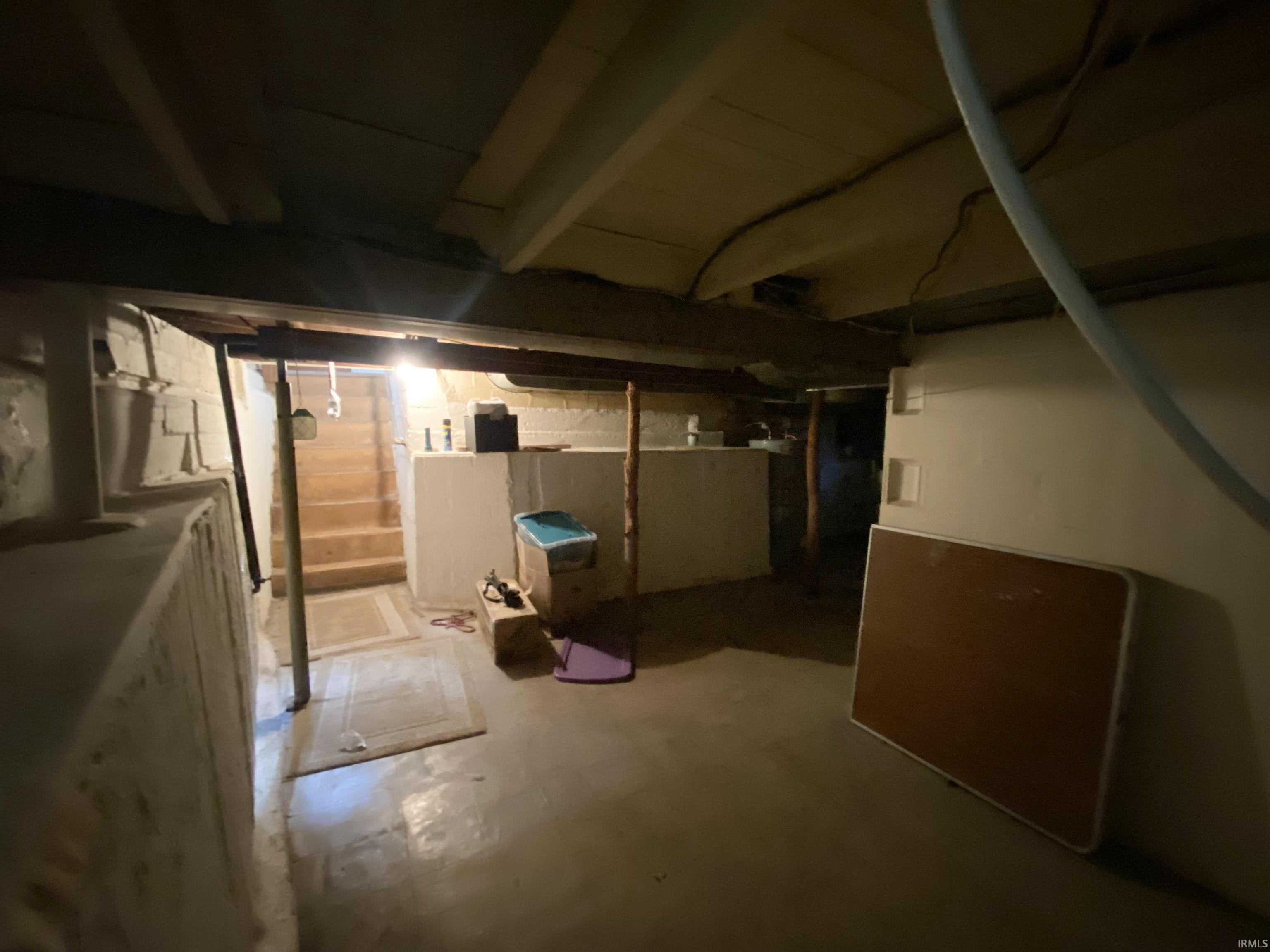 Unfinished basement space featuring exposed ceiling joists, concrete flooring, and a visible staircase providing access