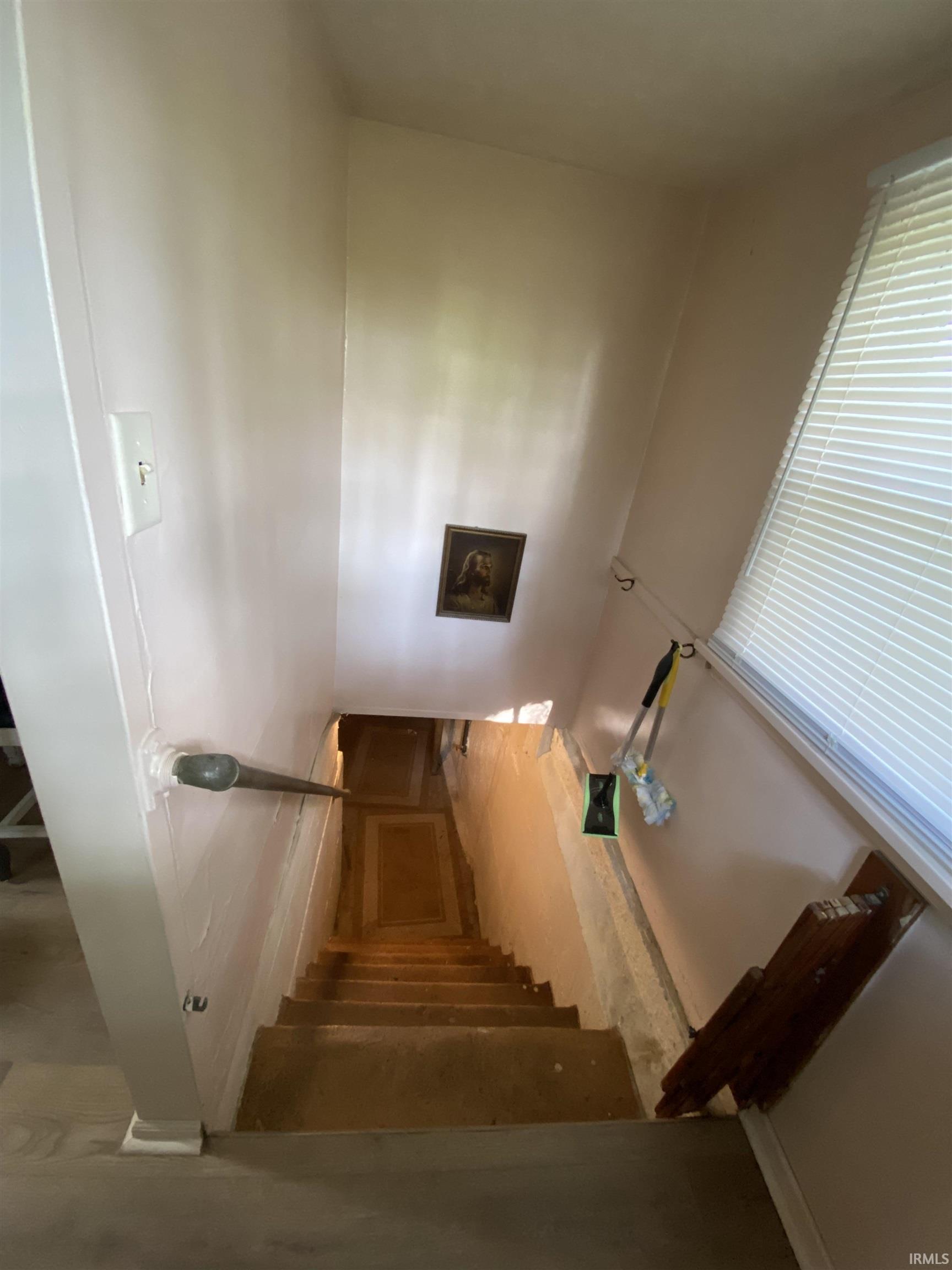 Stairwell featuring a light-colored wall finish, white trim, and a window with horizontal blinds