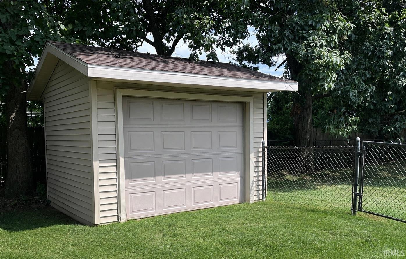 Detached garage featuring panel garage door, horizontal vinyl siding, asphalt shingle roof, and rain gutters