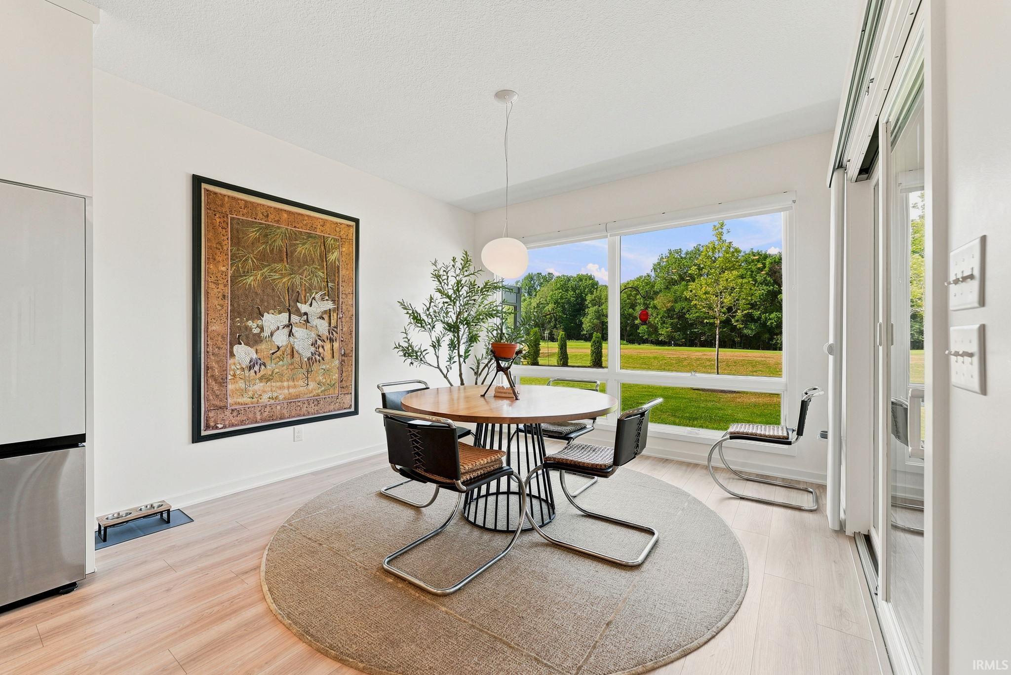 Room featuring light wood-finish flooring, white walls, and a large window presenting a green landscape