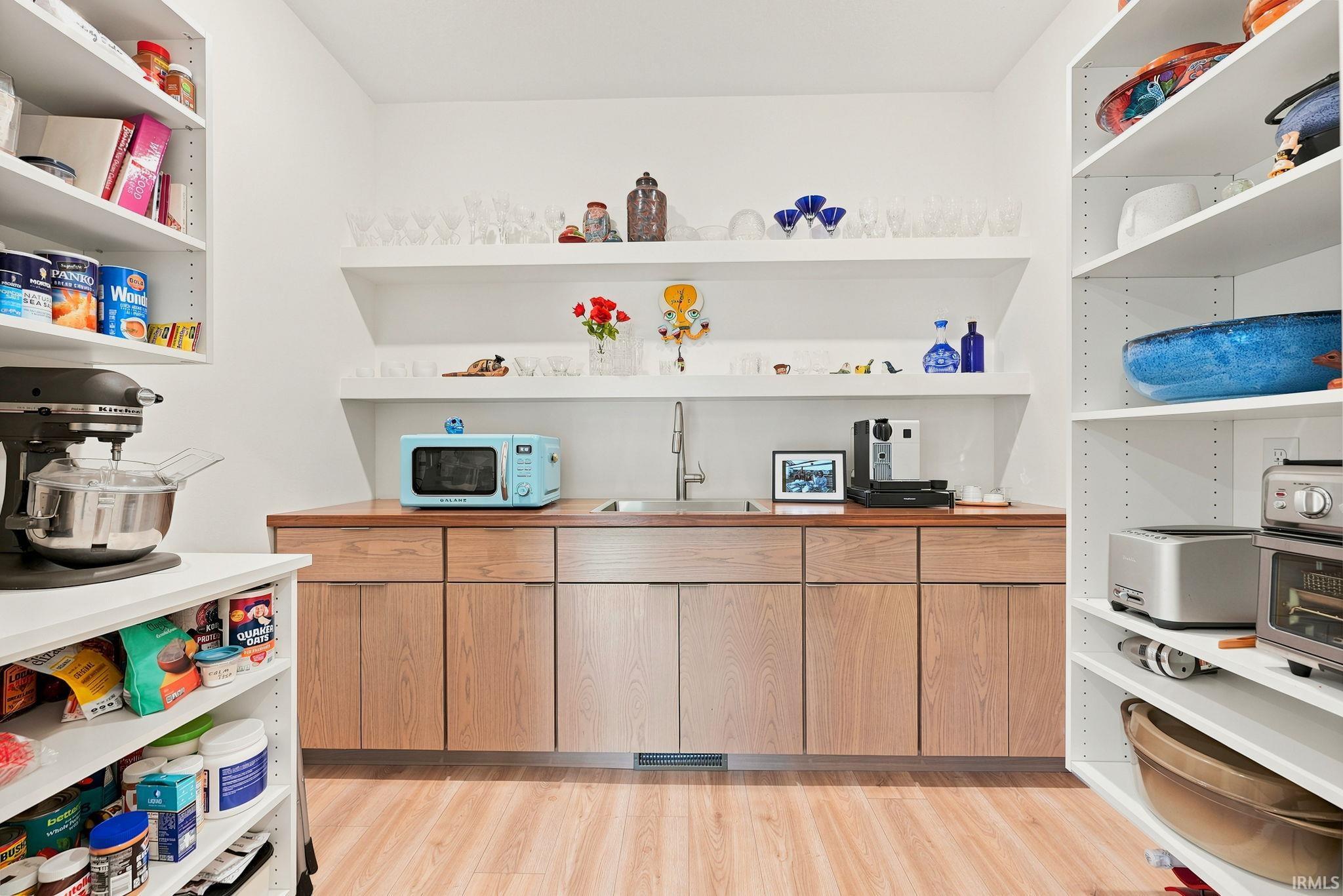 Dedicated pantry area featuring extensive built-in shelving, wood-finish flooring, a built-in sink, and custom wood cabinetry