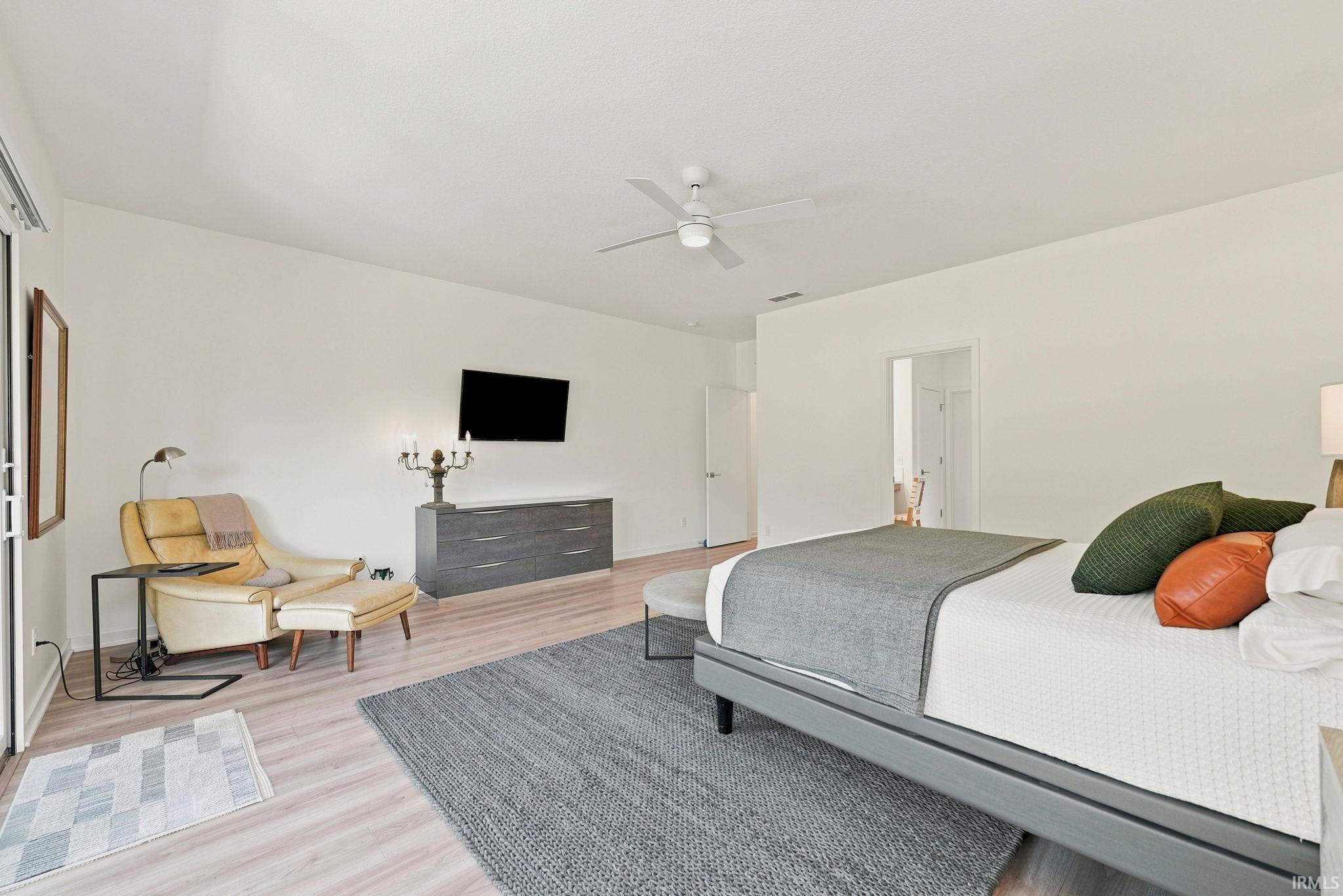 Spacious room with light wood-finish flooring, a ceiling fan, and white walls