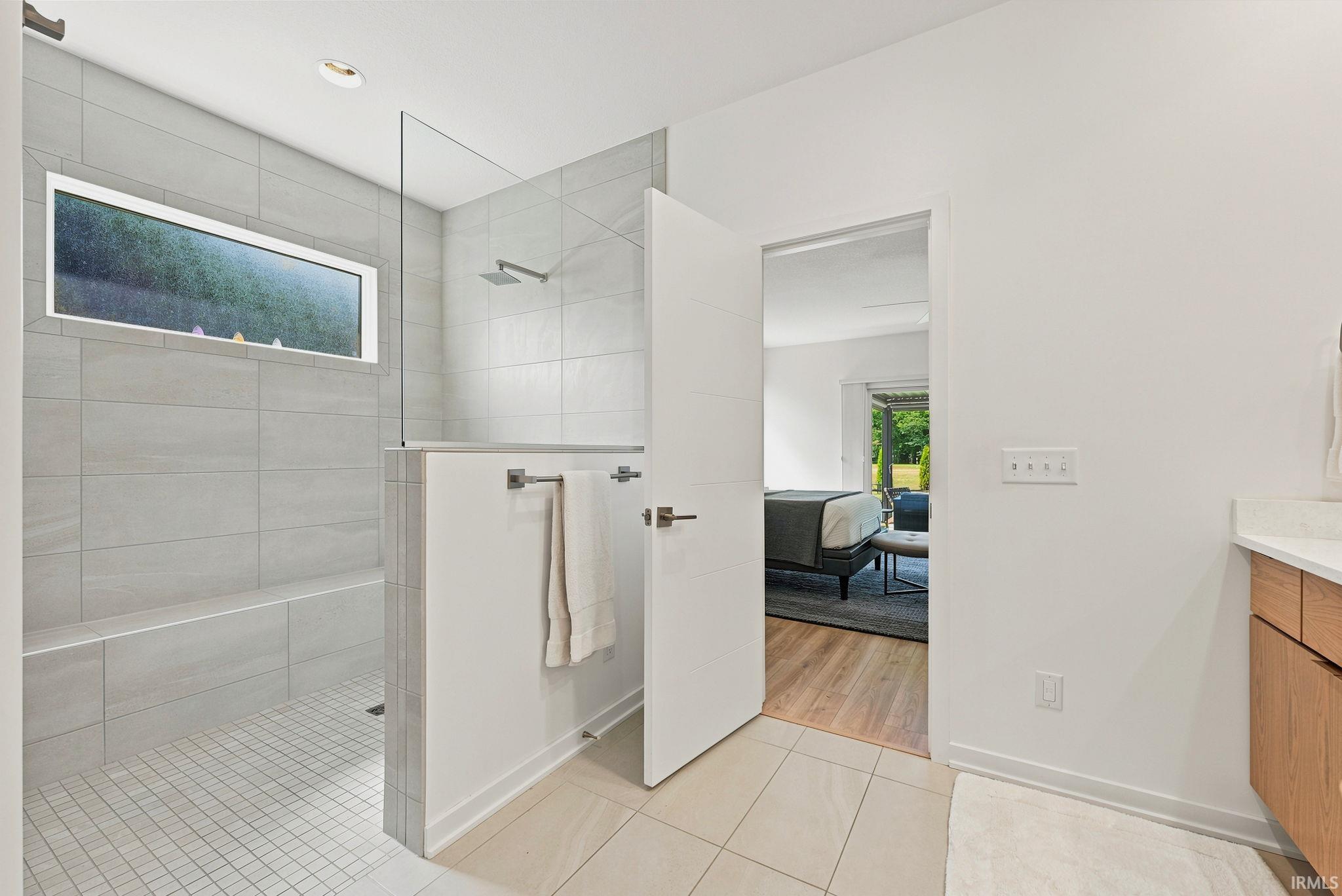Spacious shower with a glass panel enclosure, built-in bench, square tile flooring, and a rectangular window