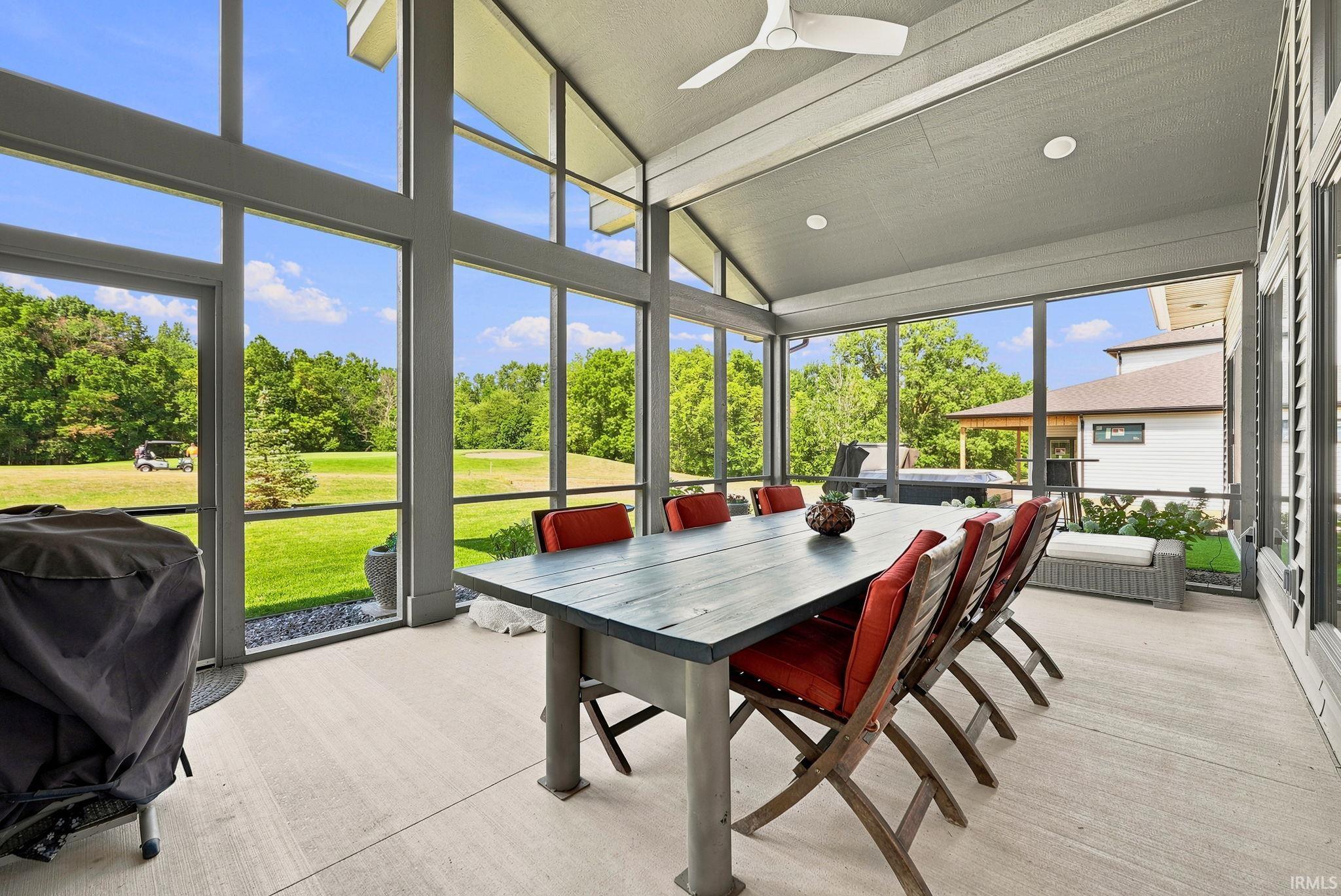 Spacious screened porch featuring a vaulted ceiling with recessed lighting and a ceiling fan, a large dining table, and extensive window walls overlooking a verdant landscape