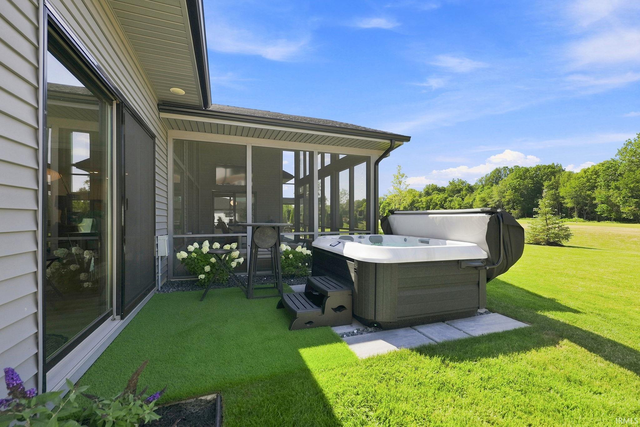 Outdoor spa area featuring a hot tub on a paver patio with steps, artificial turf, and a screened-in porch with an overhead fan