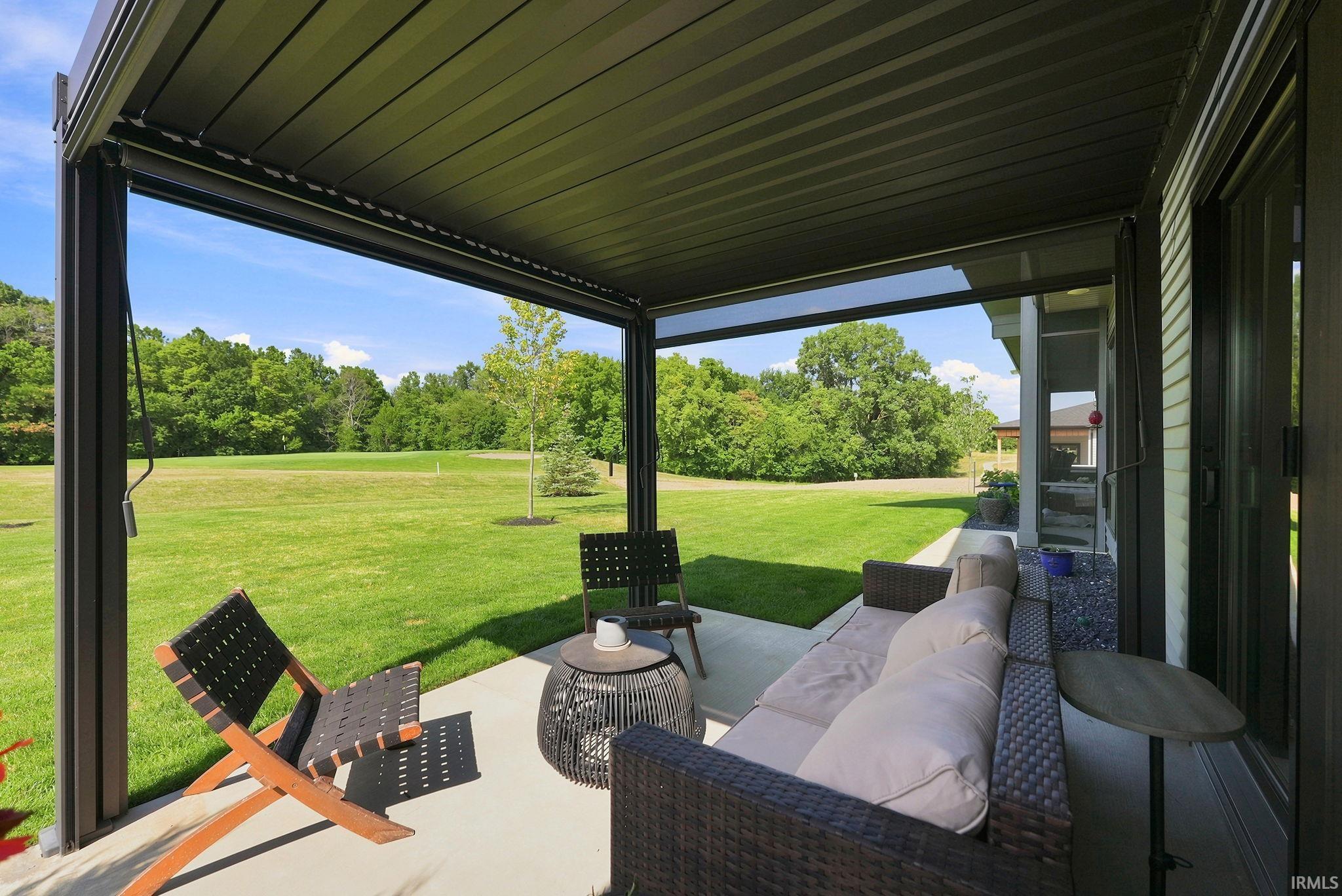 Covered patio with a dark-finished ceiling, concrete flooring, and an expansive grassy area beyond