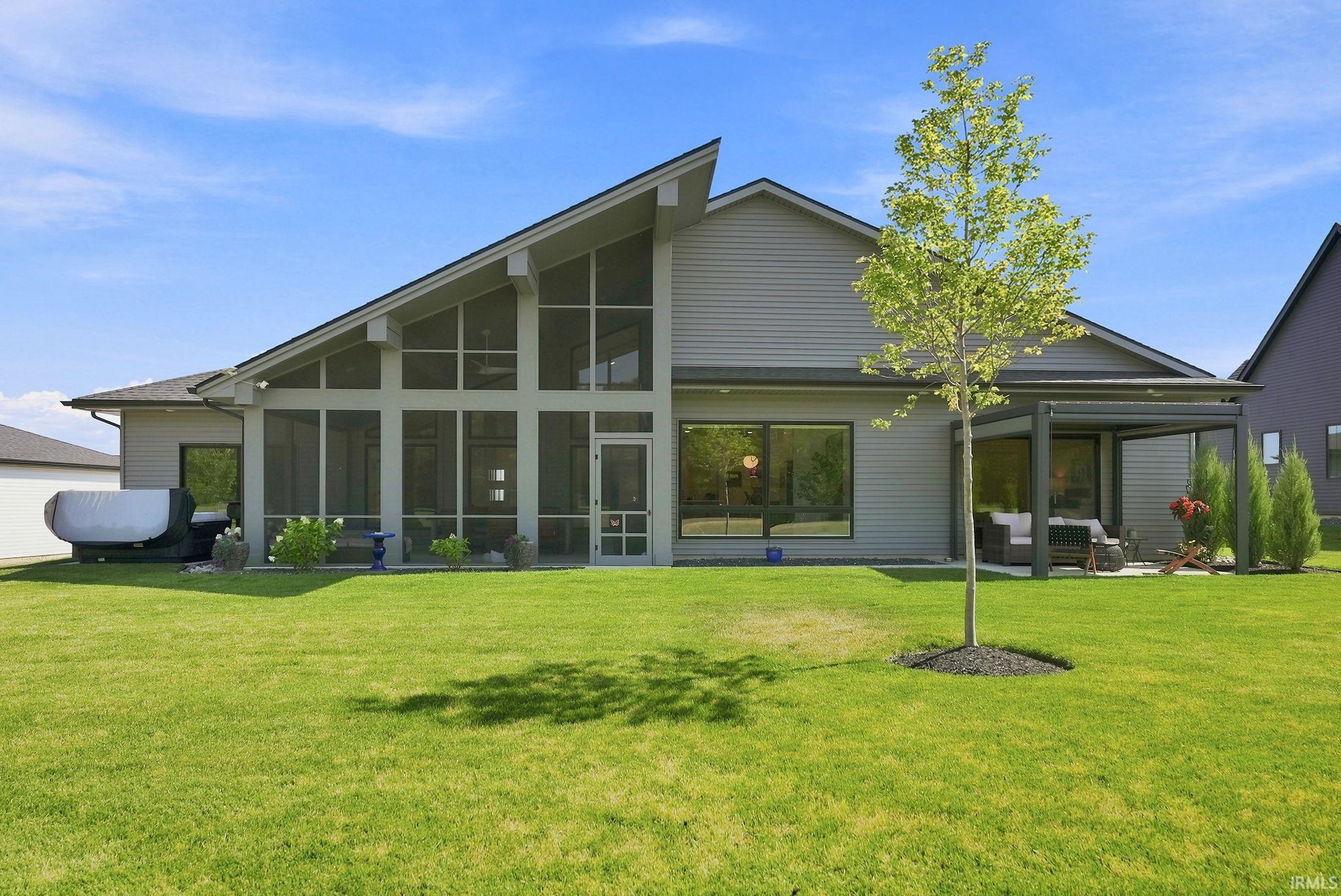 Expansive green lawn with a screened-in porch featuring a vaulted ceiling and floor-to-ceiling windows, along with a covered patio area