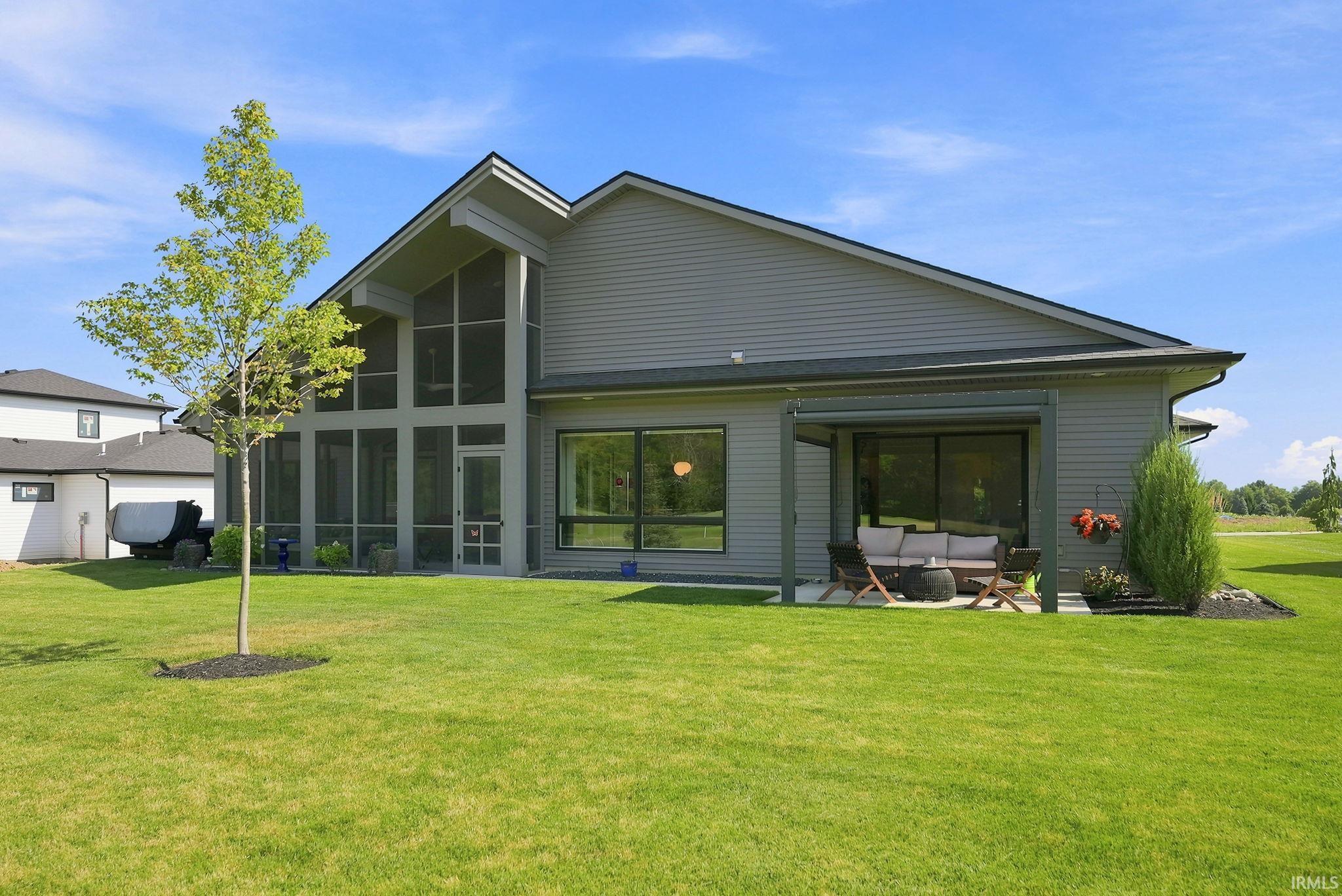 Spacious rear exterior featuring a screened-in porch with vaulted ceilings, a covered patio, and large windows