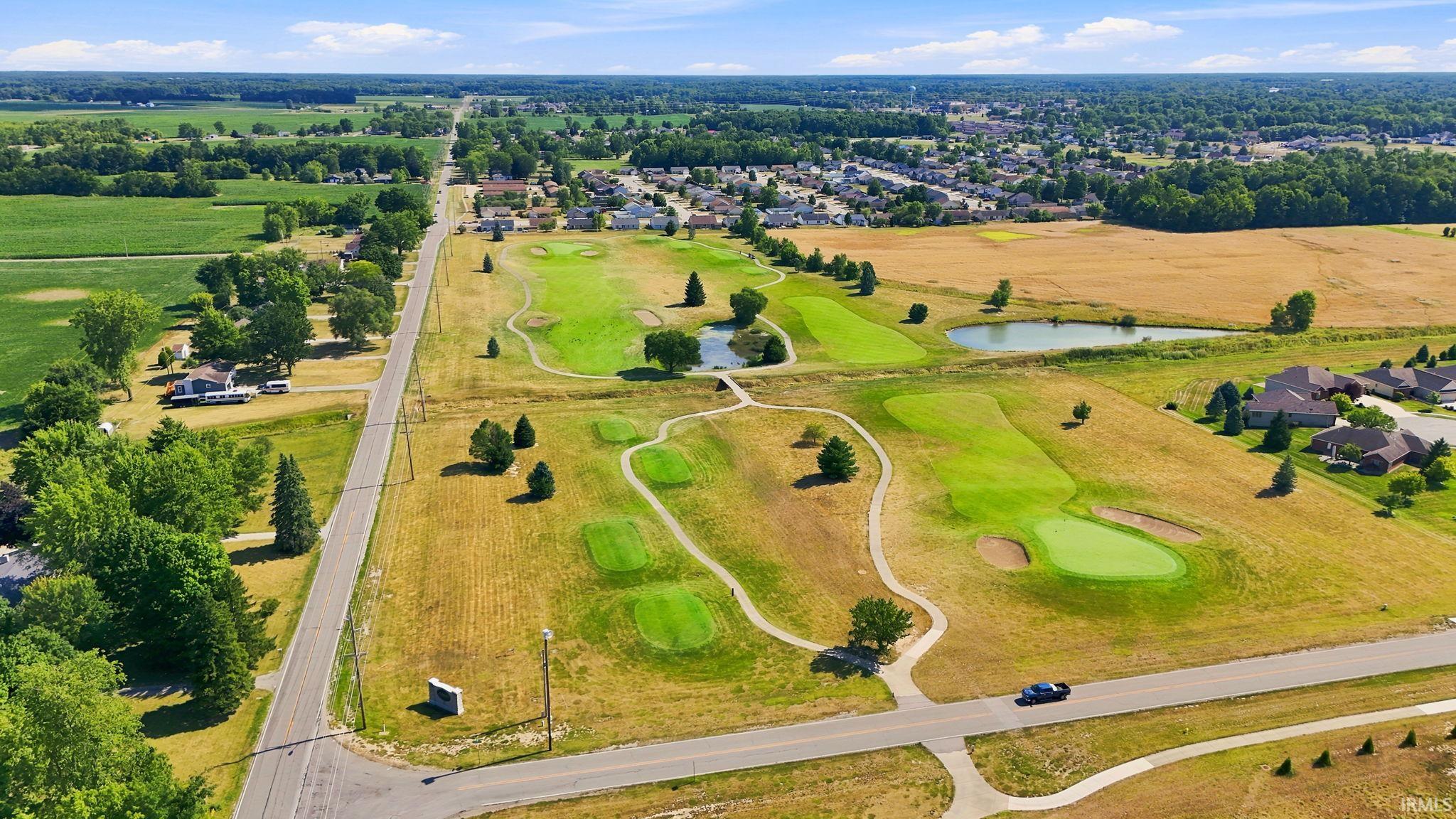 Expansive property featuring a golf course, multiple residential structures, agricultural fields, and paved roadways, all under a clear sky