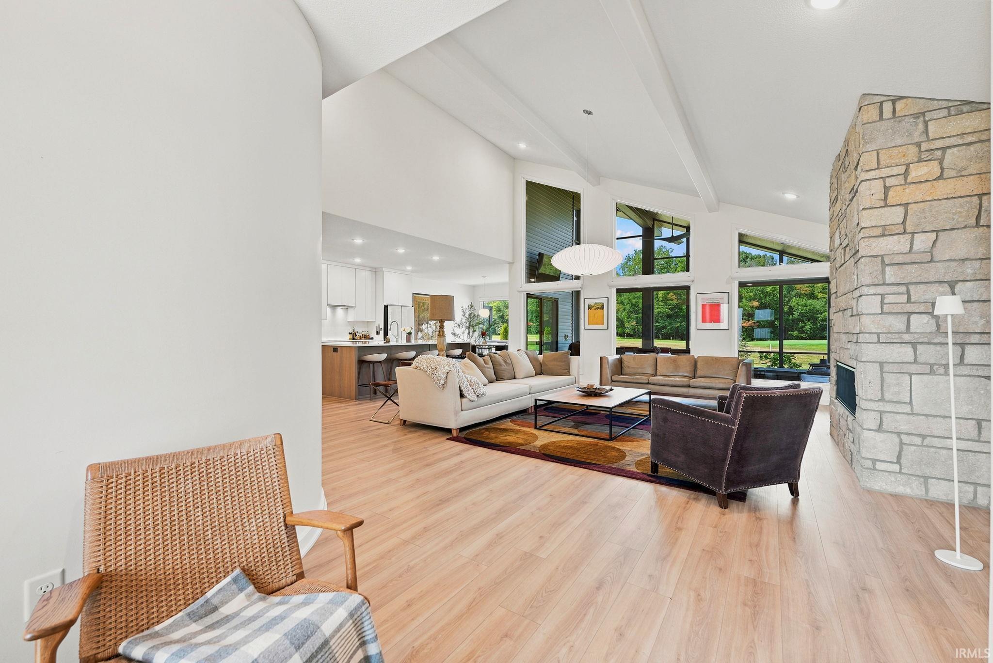Expansive living area featuring vaulted ceilings, wood-finish flooring, a stone fireplace, and abundant natural light from large windows