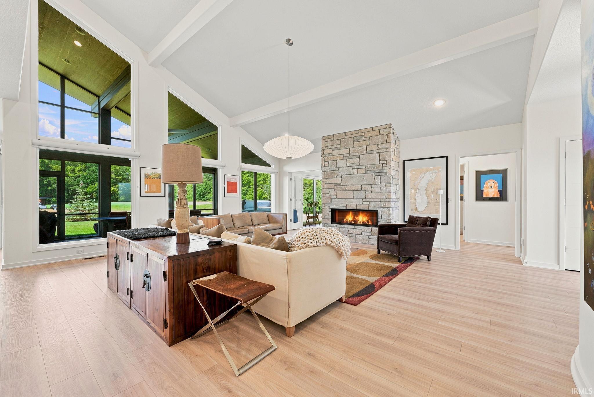 Expansive living space featuring light wood-finish flooring, a stone-clad fireplace with an integrated linear firebox, and a vaulted ceiling with exposed beams