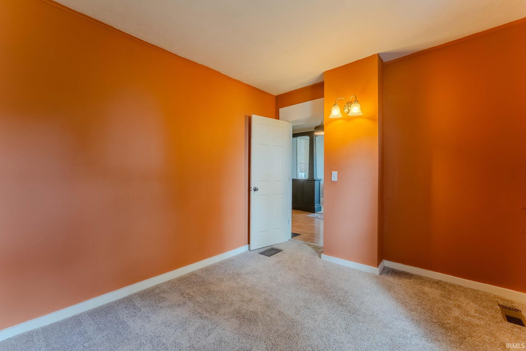 Carpeted room featuring an interior door, white baseboards, and a wall-mounted sconce light fixture