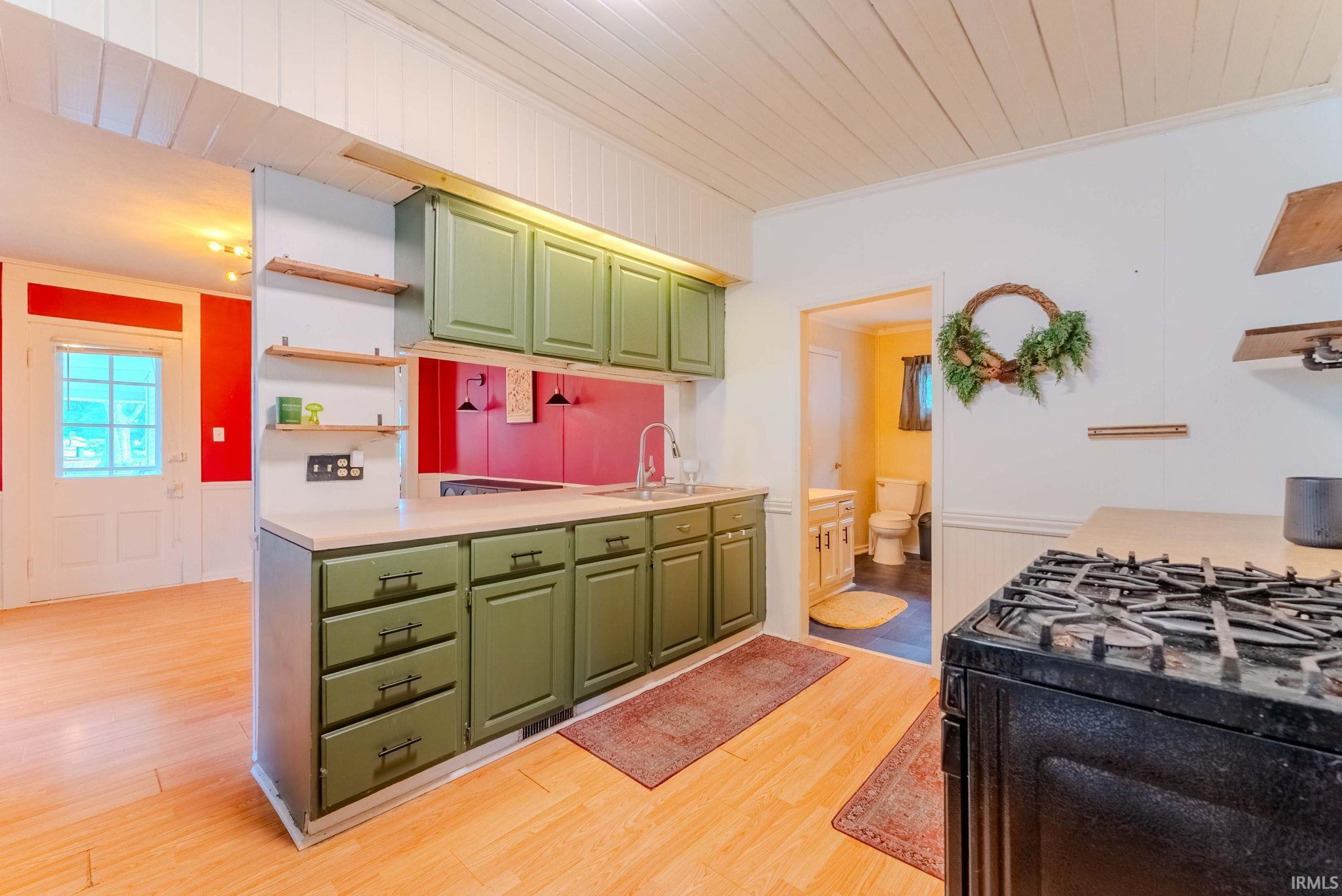 Kitchen featuring olive green cabinetry, light-toned countertops, and wood-finish flooring