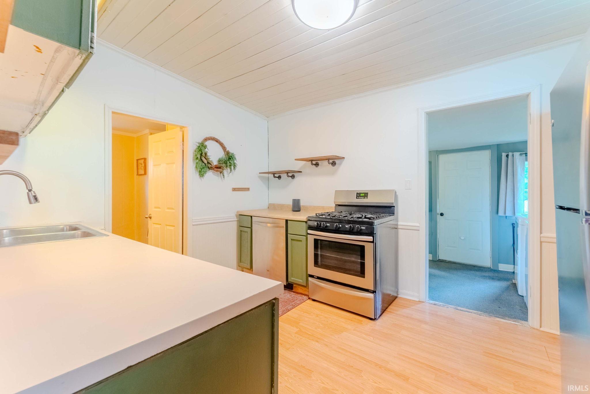 Kitchen featuring wood-finish flooring, stainless steel appliances, light countertops, and green base cabinetry