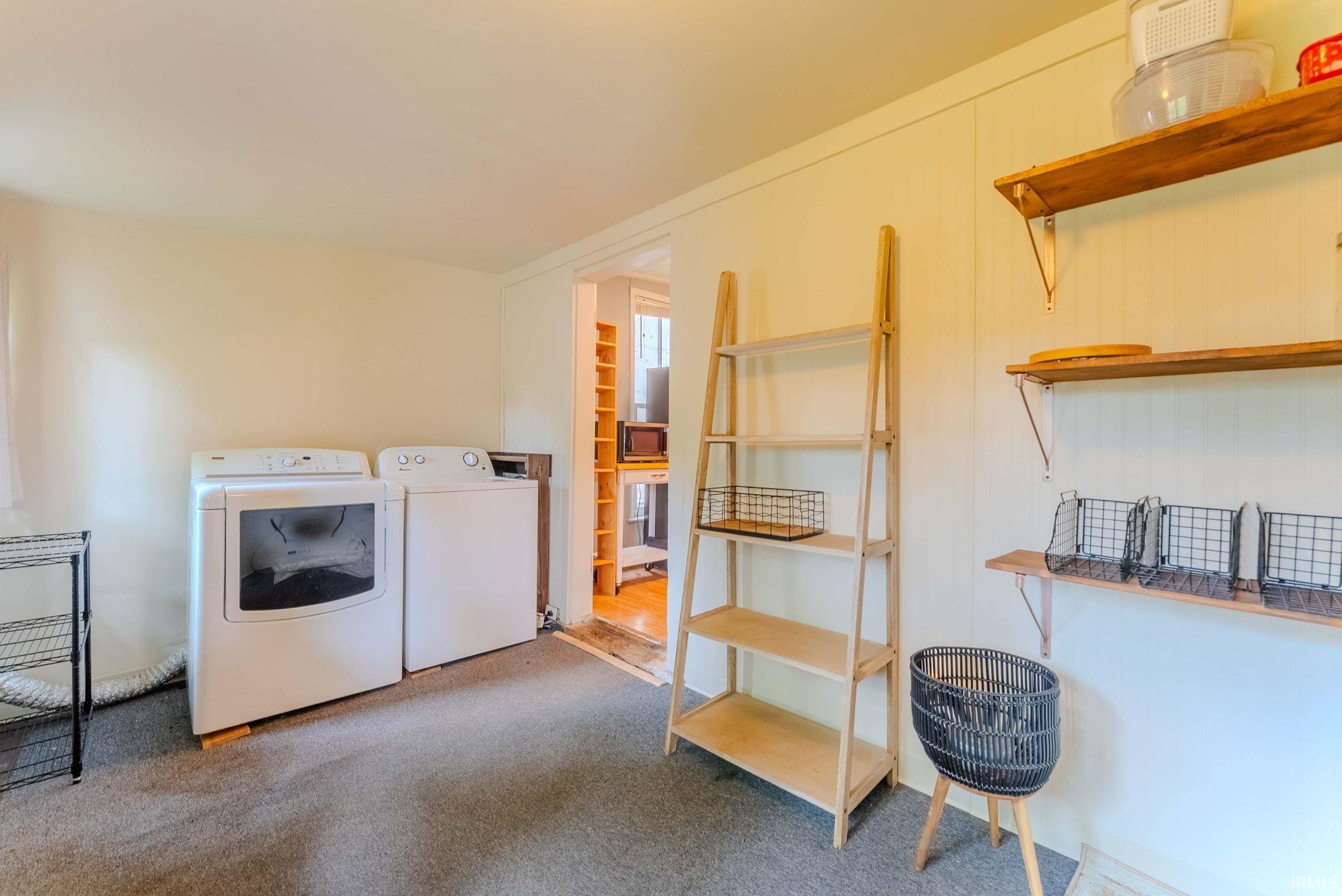 Dedicated laundry area featuring a washer and dryer, wood-finish shelving, and overhead storage