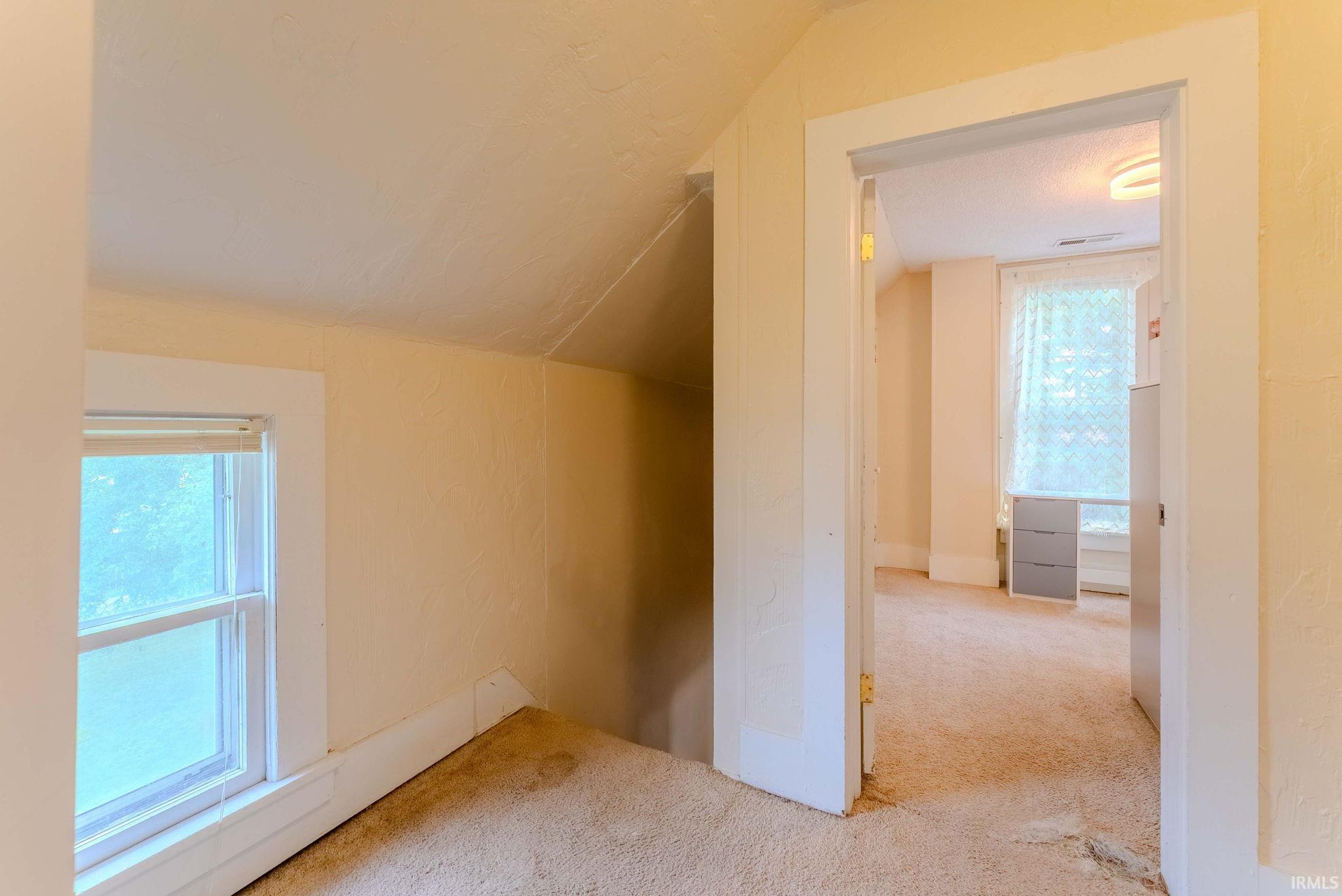 Carpeted attic space featuring a double-hung window with white trim, offering natural light