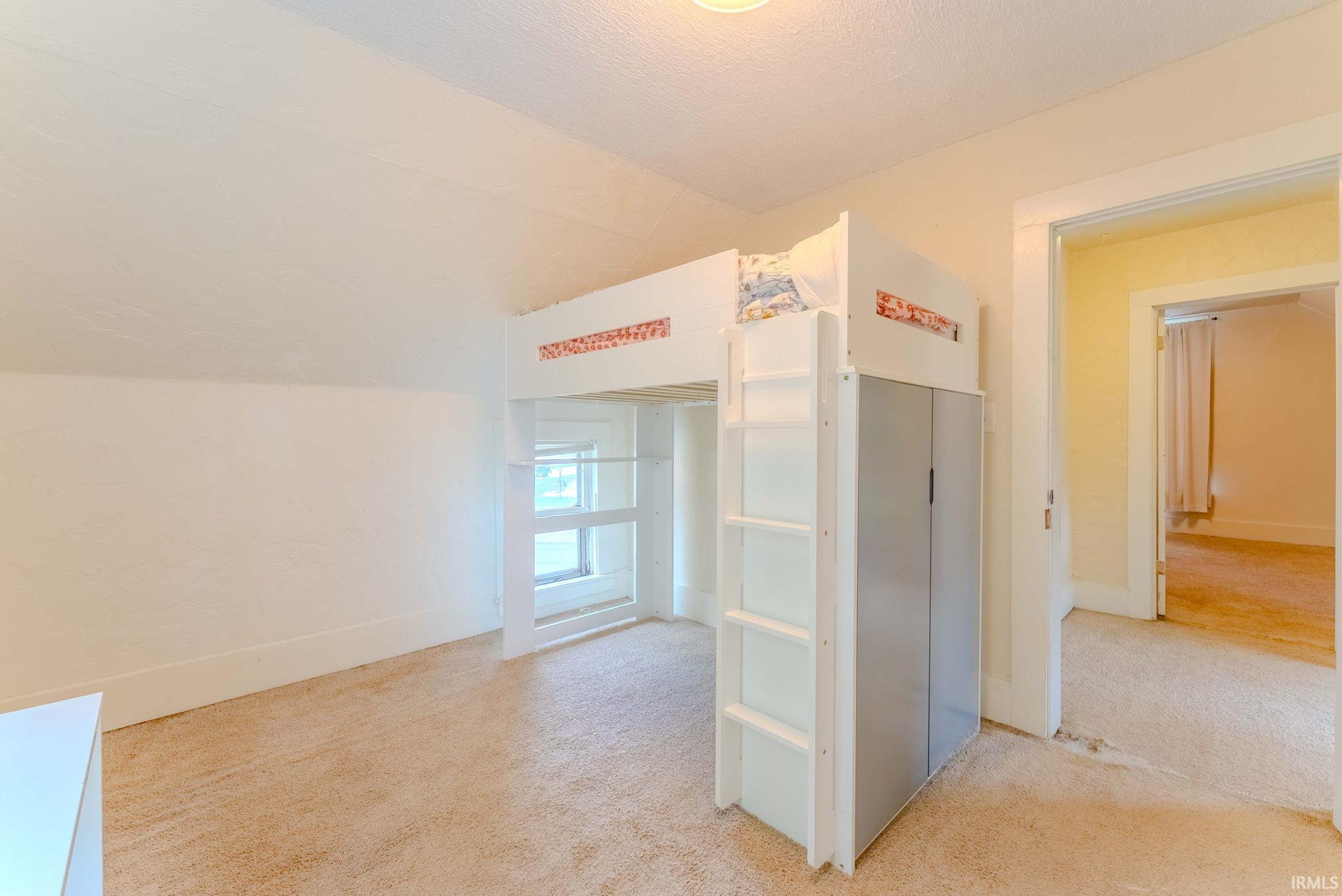 Bedroom space featuring a window, sloped ceiling, and plush carpet flooring