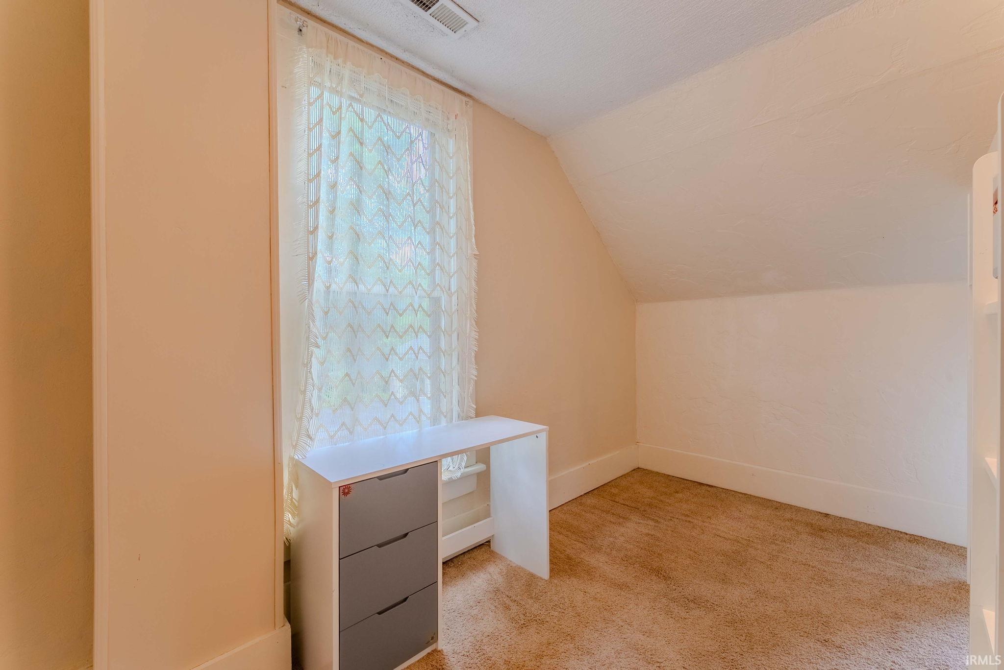 Room featuring an angled ceiling, light-colored walls, and carpeting