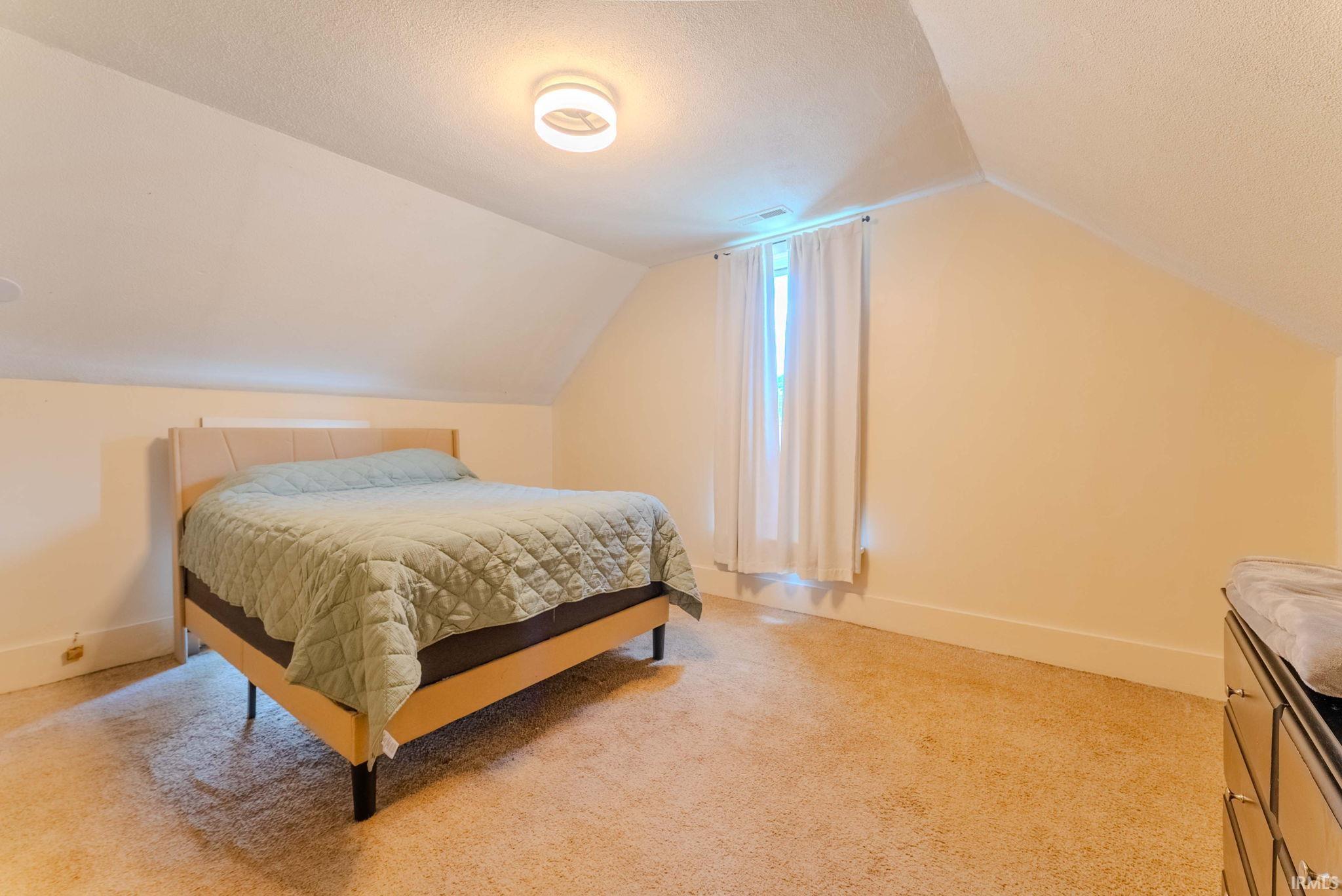 Carpeted room featuring a sloped ceiling and a window with white curtains