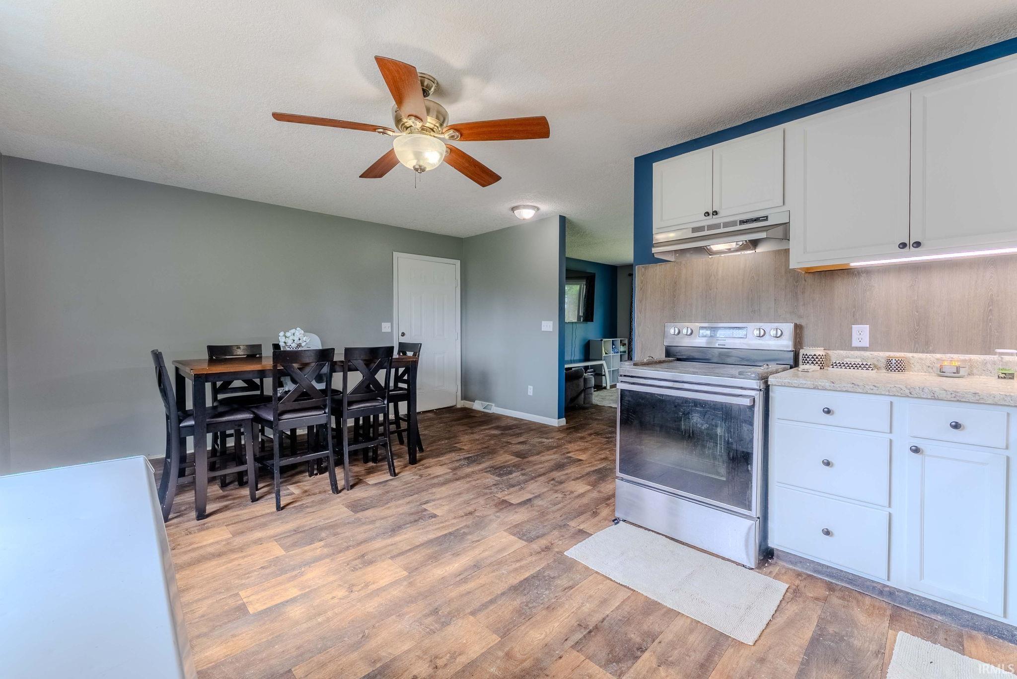 Open-concept kitchen and dining area featuring wood-finish flooring, light-toned cabinetry, stainless steel range, and a ceiling fan with light fixture