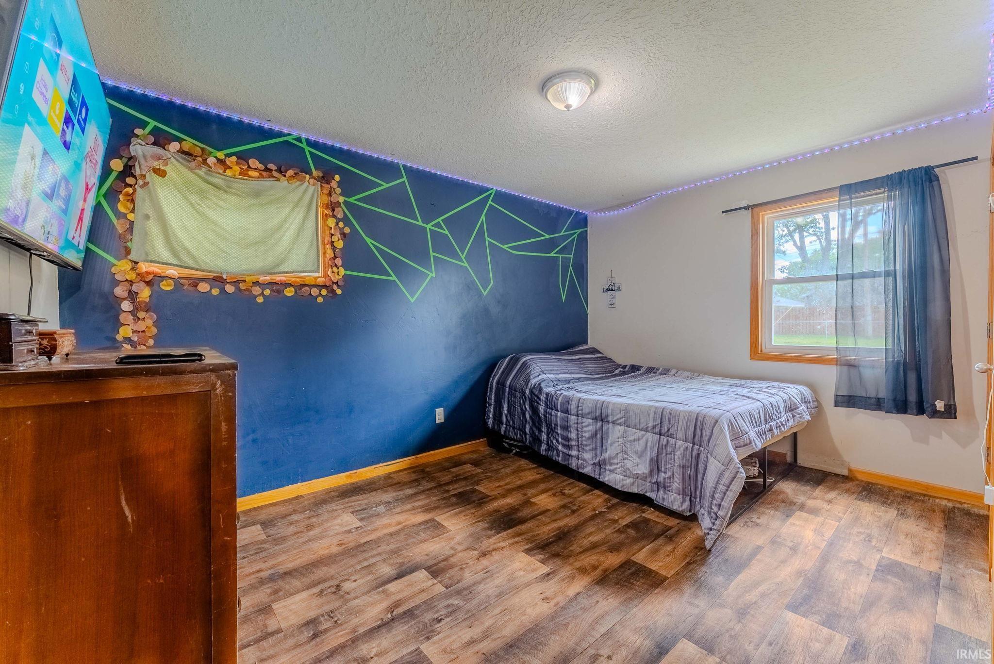 Room featuring wood-finish flooring, a single window with natural wood trim, and a ceiling-mounted light fixture