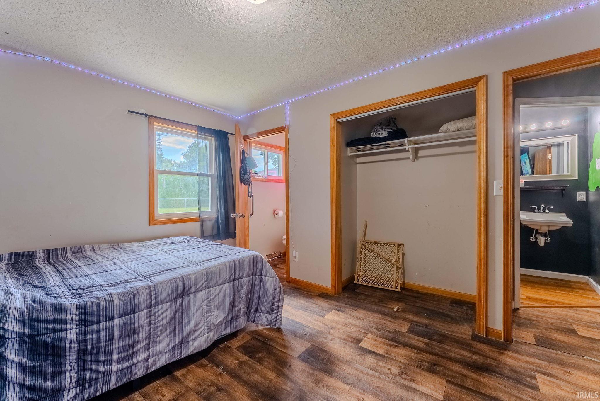 Room featuring wood-finish flooring, a window with natural light, a built-in closet with shelving, and a doorway leading to a bathroom with a pedestal sink and vanity lighting