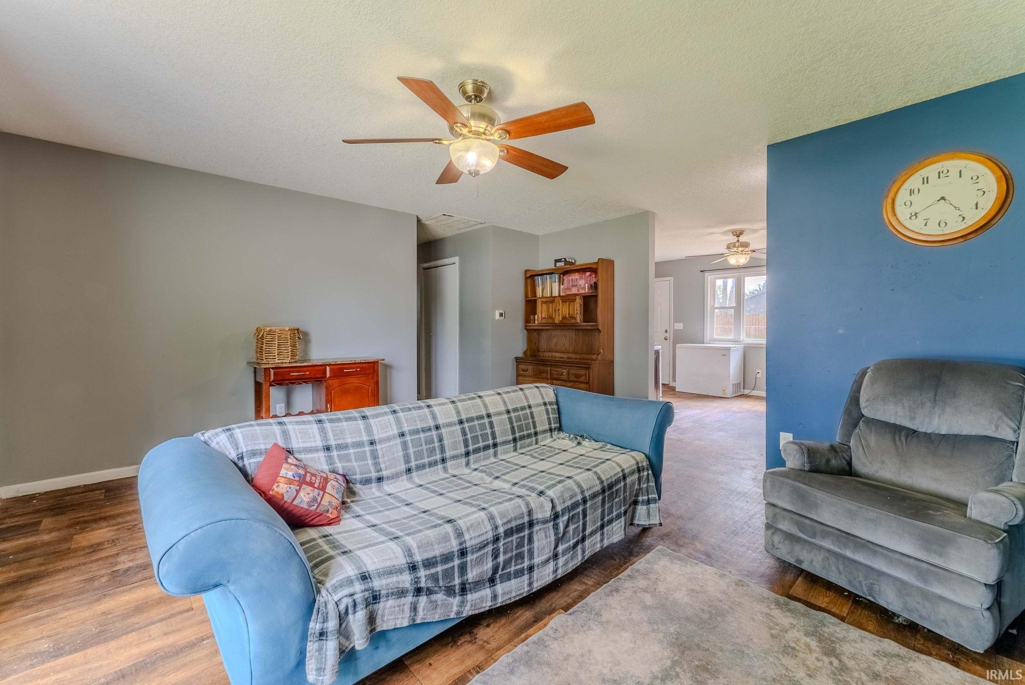 Living area featuring wood-finish flooring, a ceiling fan with integrated lighting, and a neutral wall color palette