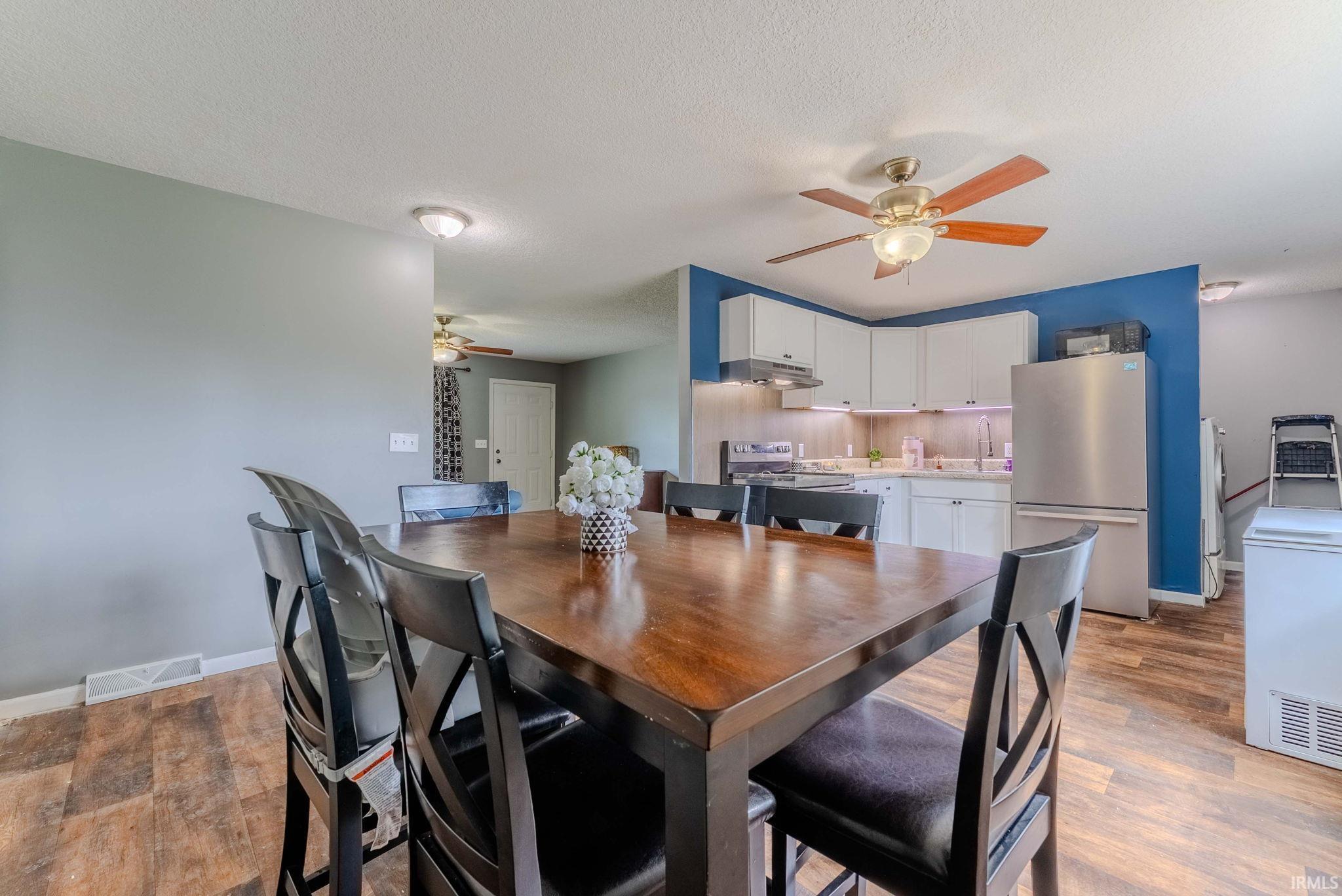 Spacious kitchen and dining area featuring wood-finish flooring, white cabinetry, stainless steel appliances, and a ceiling fan with integrated lighting